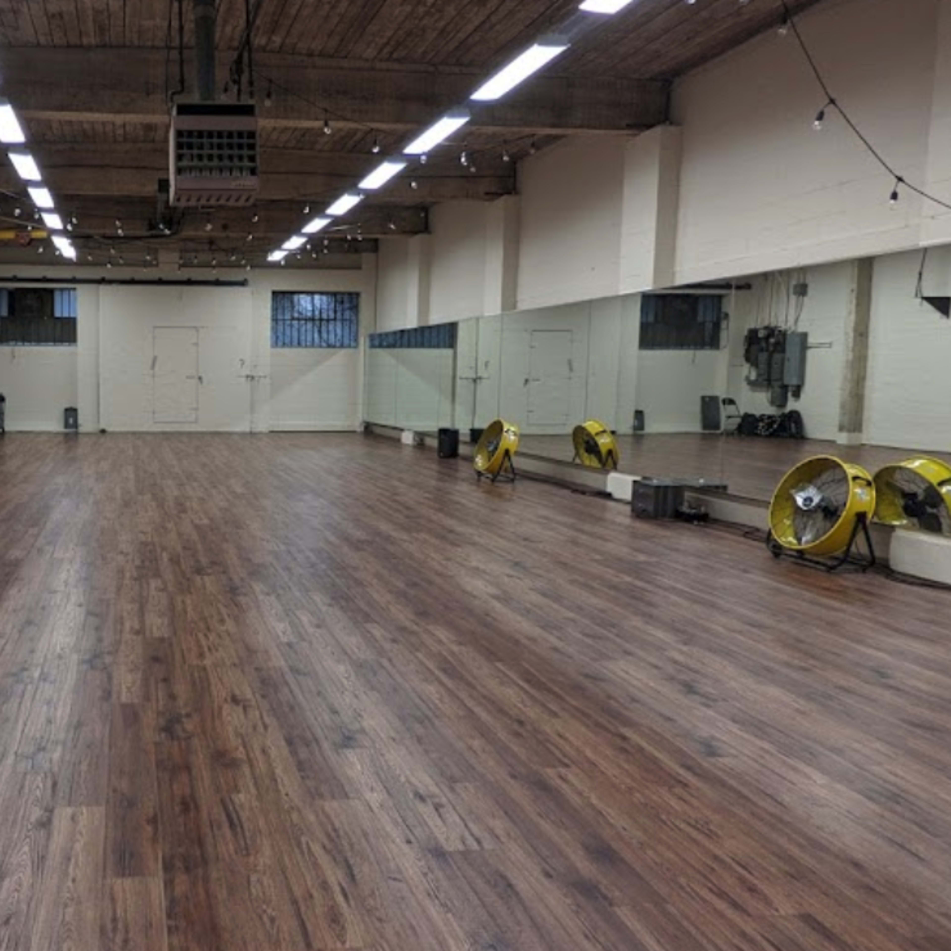 A spacious, empty room with wooden flooring and large mirrors on one wall.