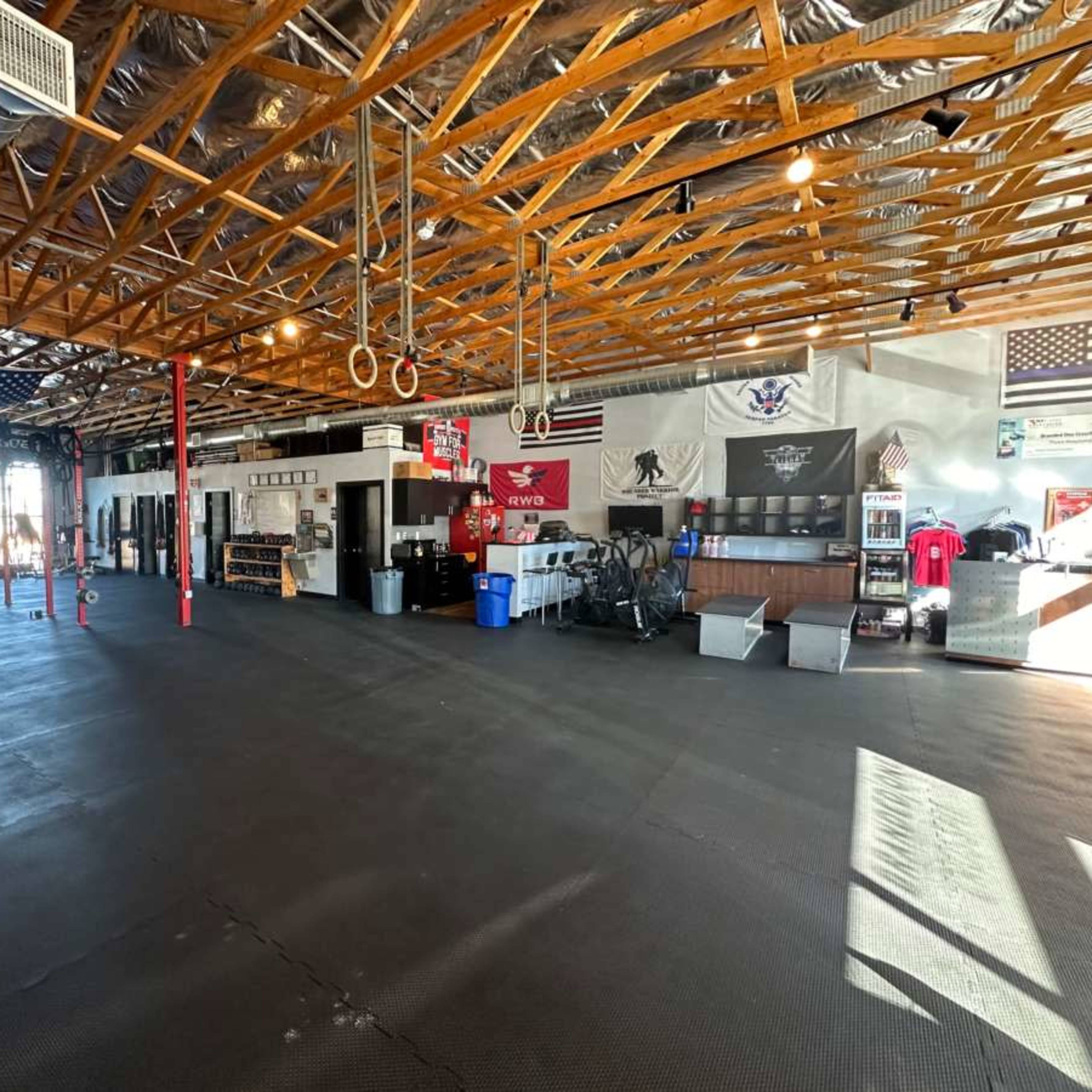 An indoor gym with a spacious floor, exposed wooden beams, various workout equipment, and several flags displayed on the walls.