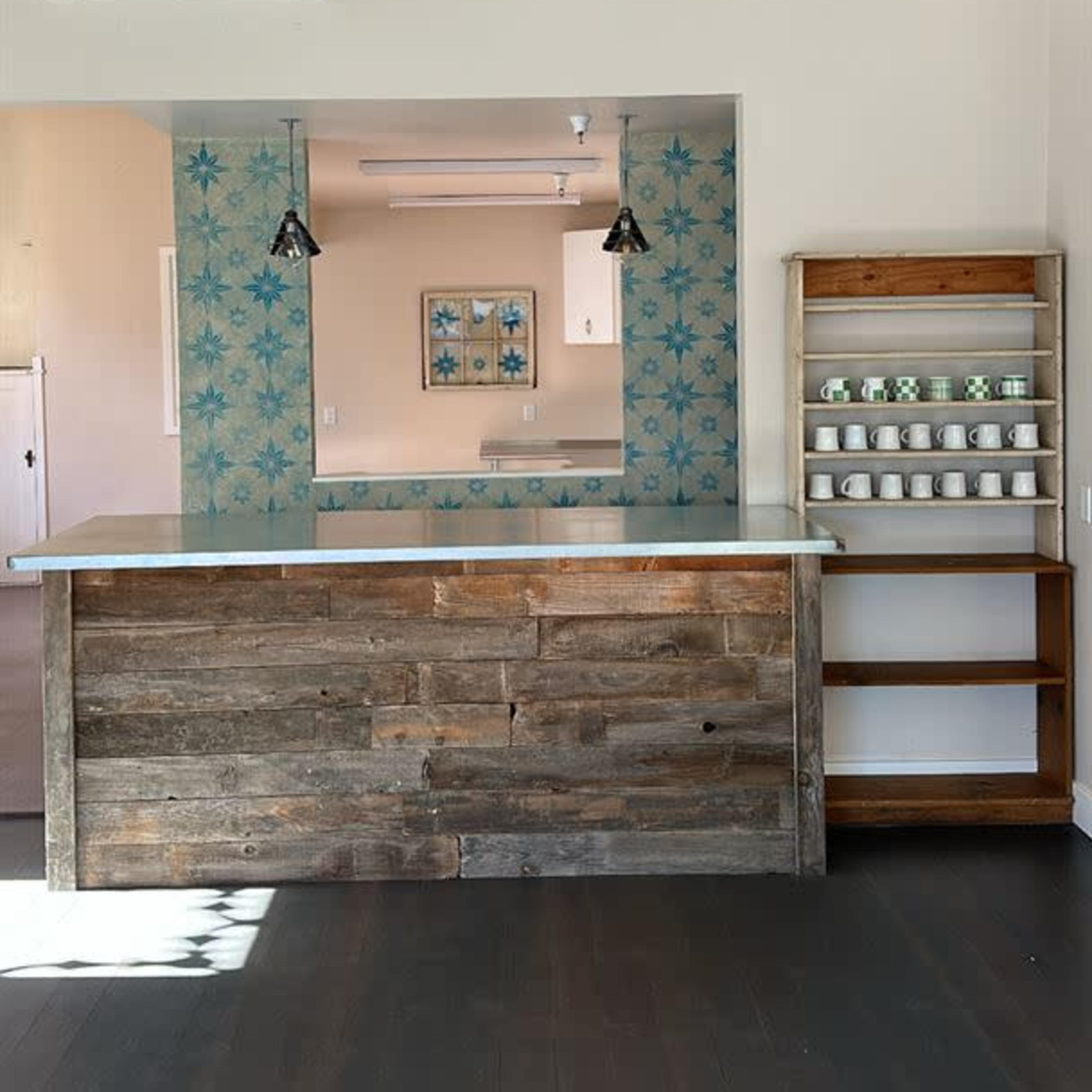 A wooden counter with a back wall featuring blue patterned tiles and a shelf displaying white cups.