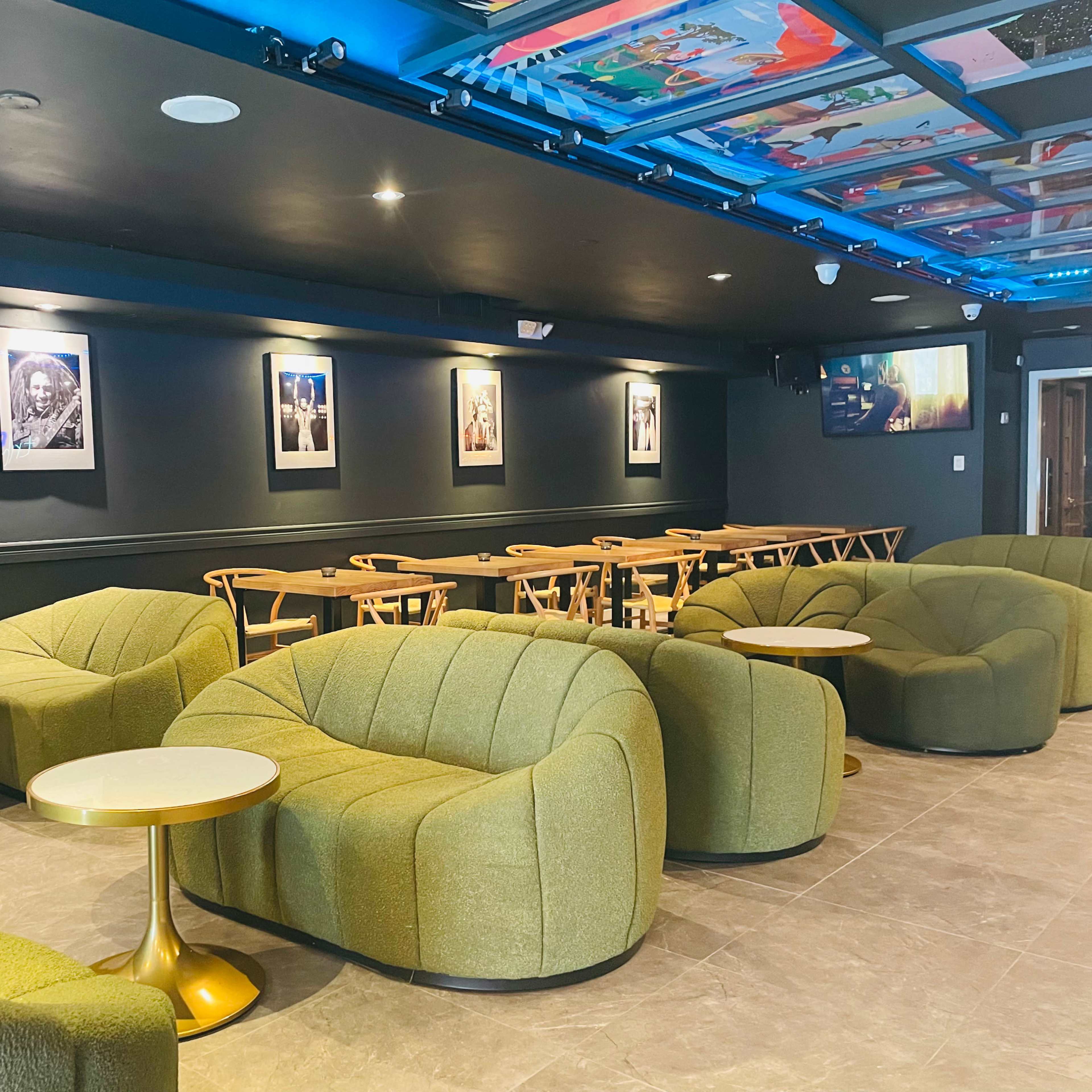 A modern lounge features green upholstered seating, round tables, and framed artwork on the walls.