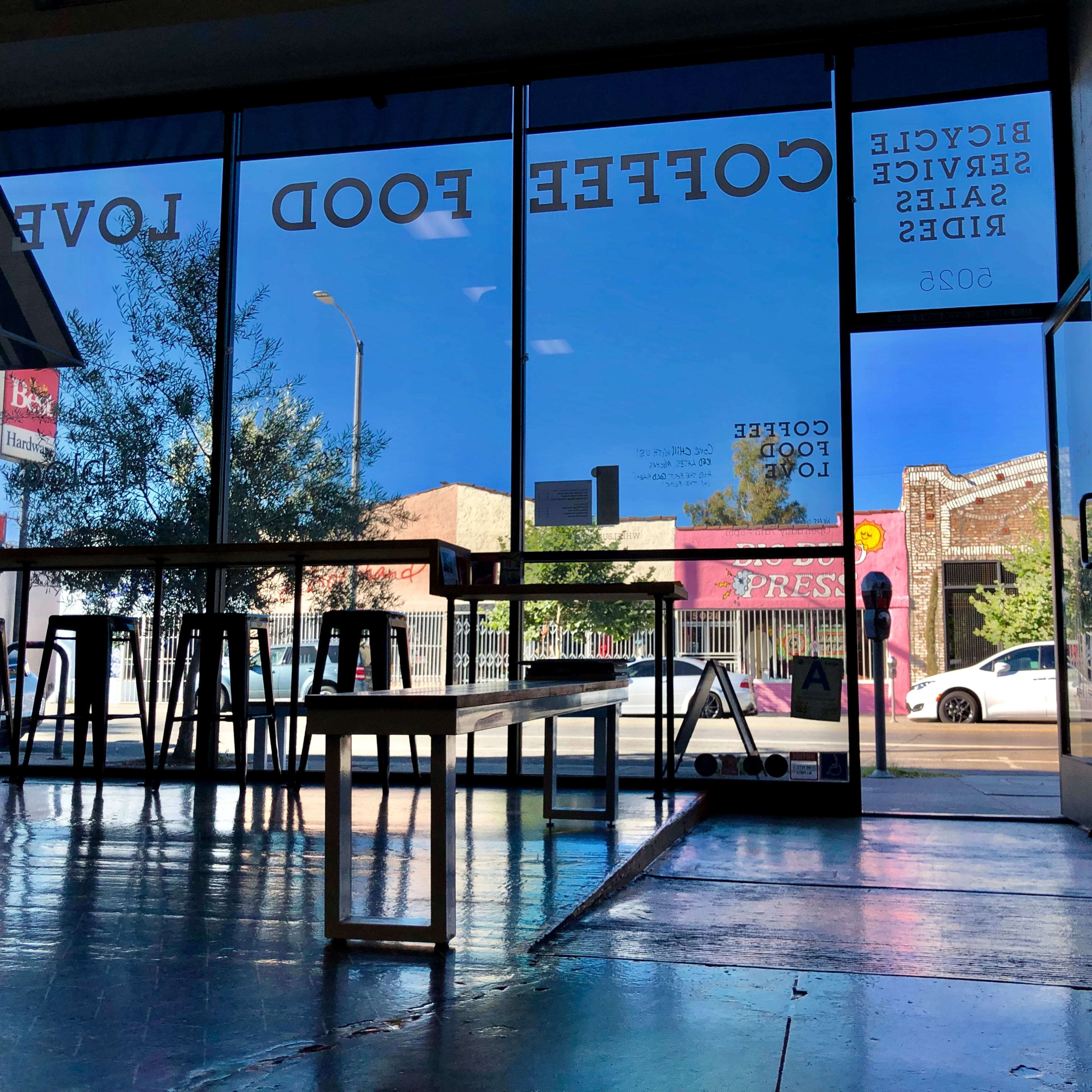 A café interior with large windows displaying a street scene and signage on the glass indicating "Coffee Food Love."