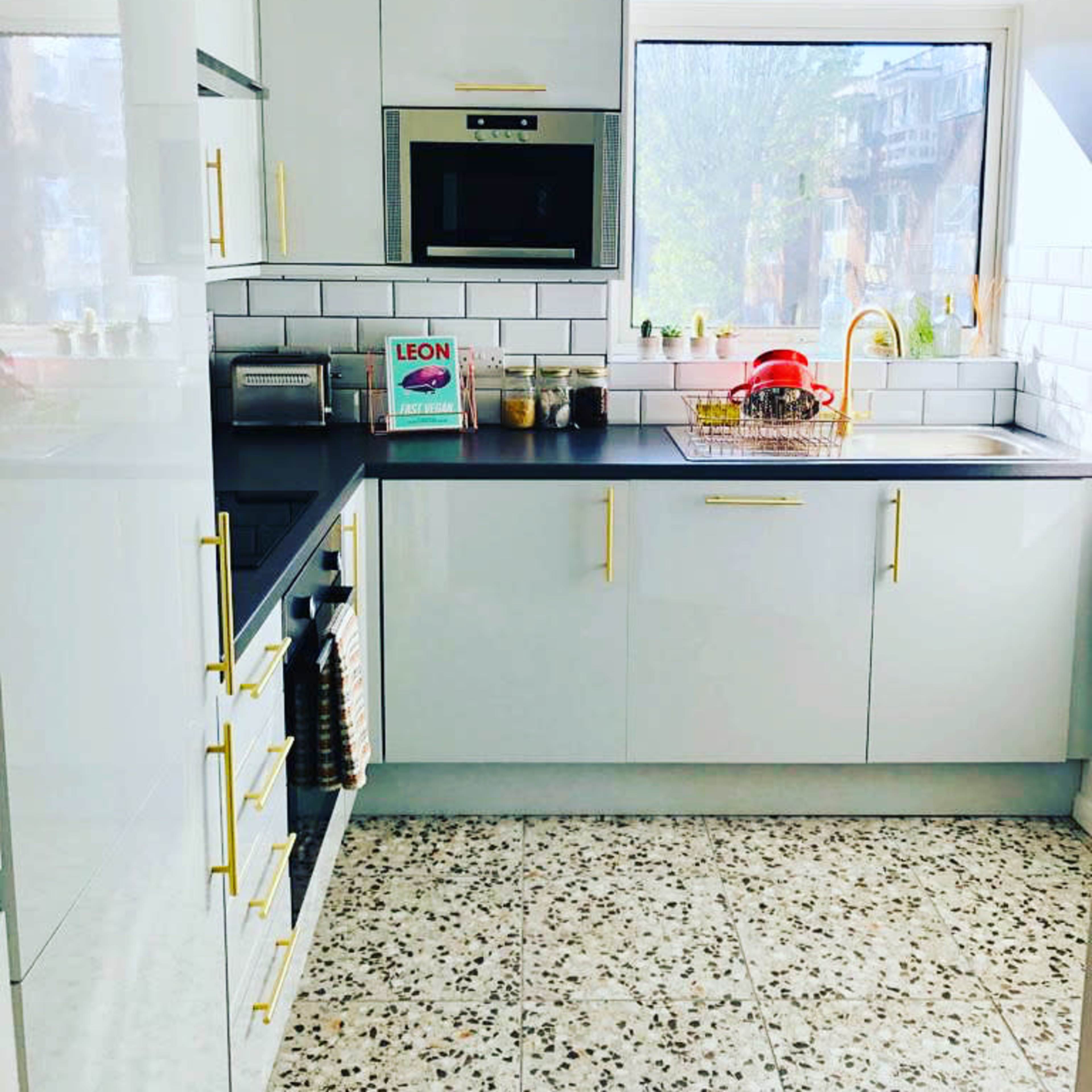A modern kitchen features white cabinetry, a microwave, and a sink with a golden faucet, set against a backdrop of patterned tile flooring.