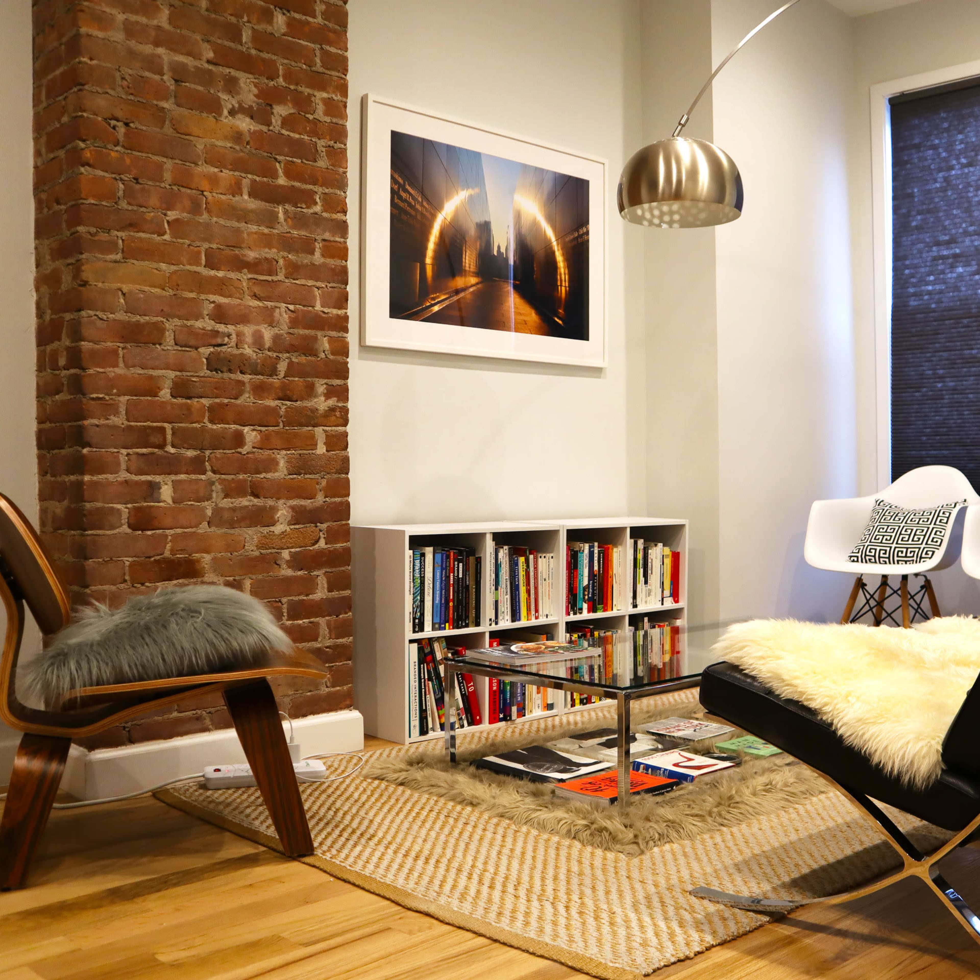 A modern living room featuring a brick wall, a bookshelf filled with books, a sleek chair, and a coffee table adorned with magazines.