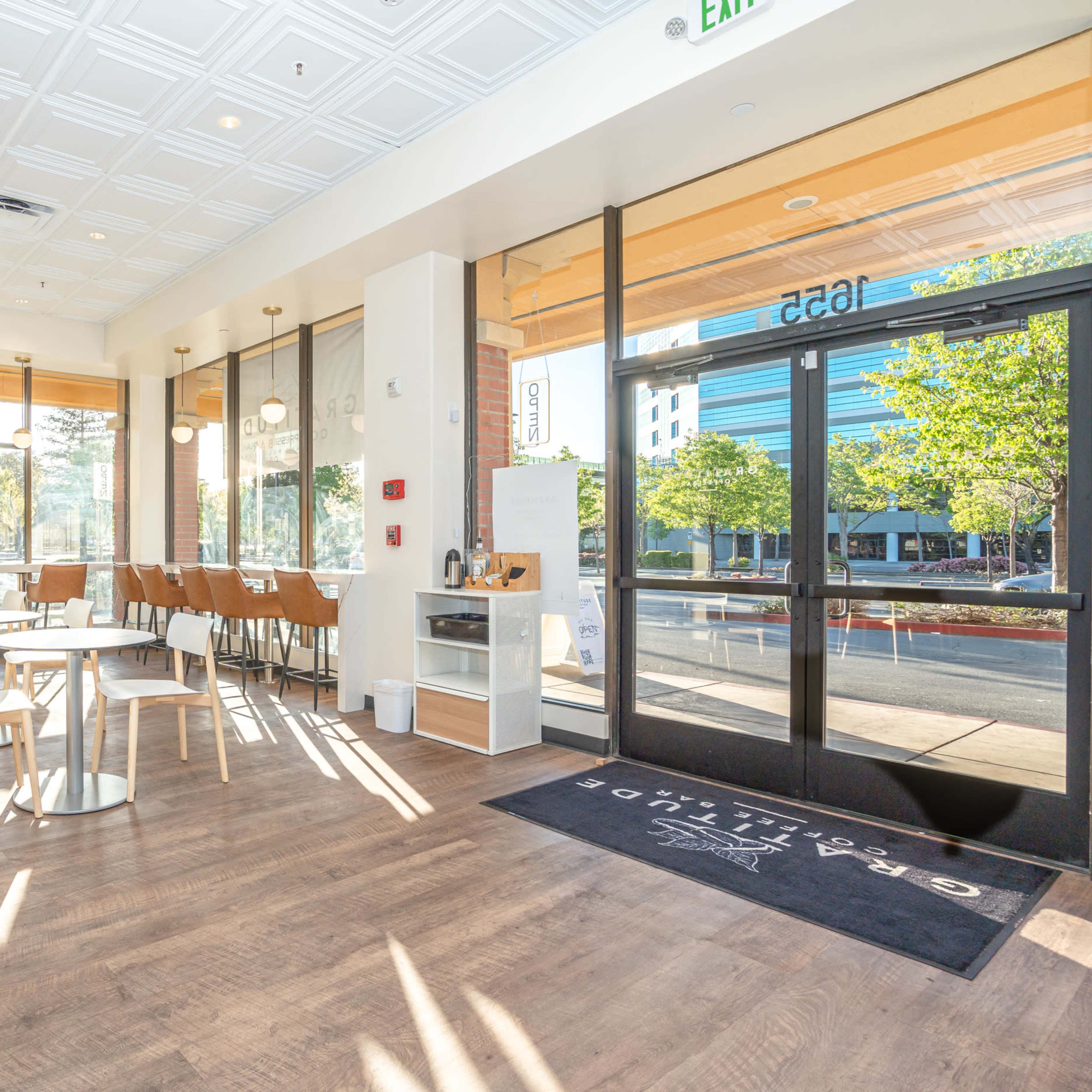 A bright, modern cafe interior with wooden flooring, large windows, and a mix of tables and chairs.