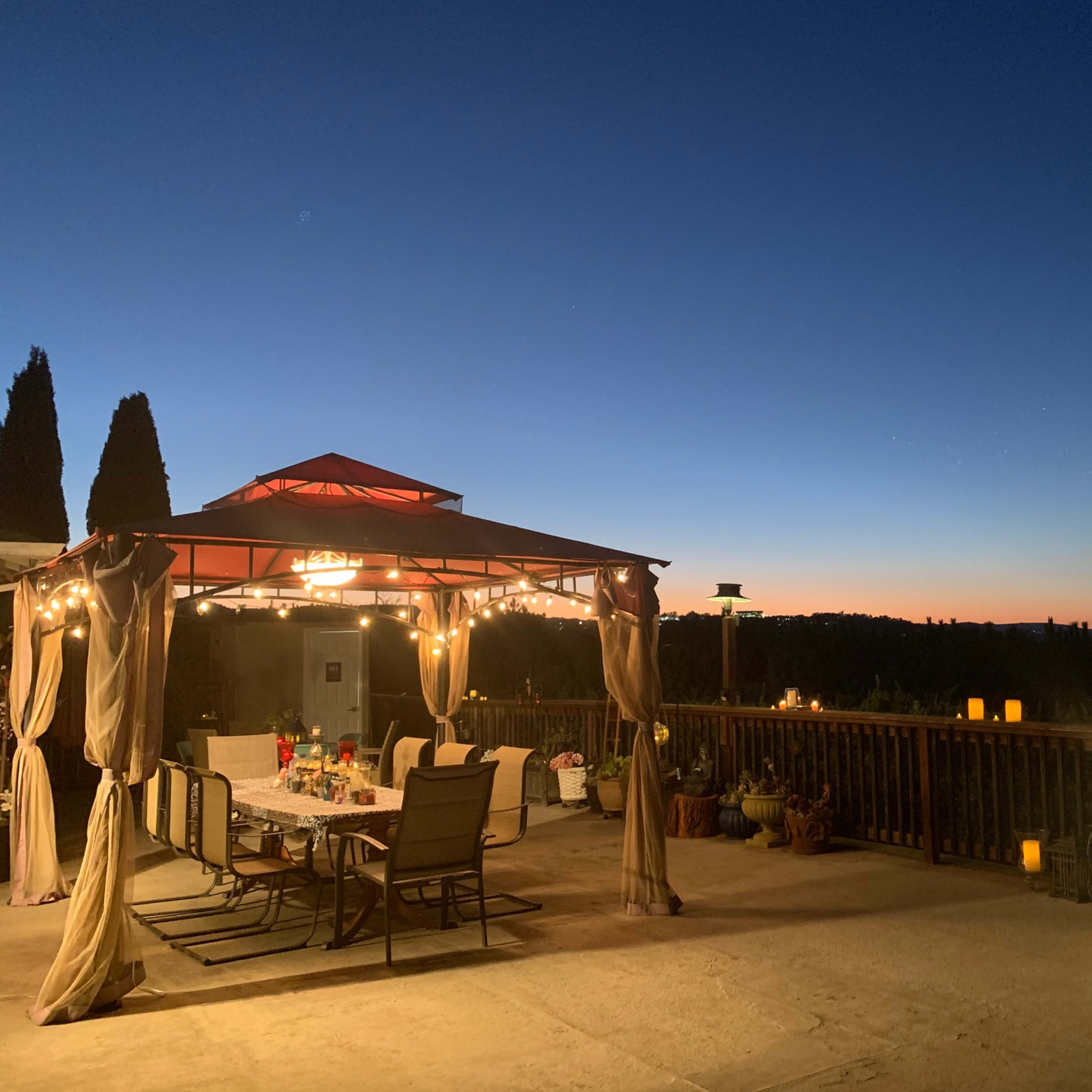 A covered outdoor dining area is illuminated by string lights, set against a twilight sky.