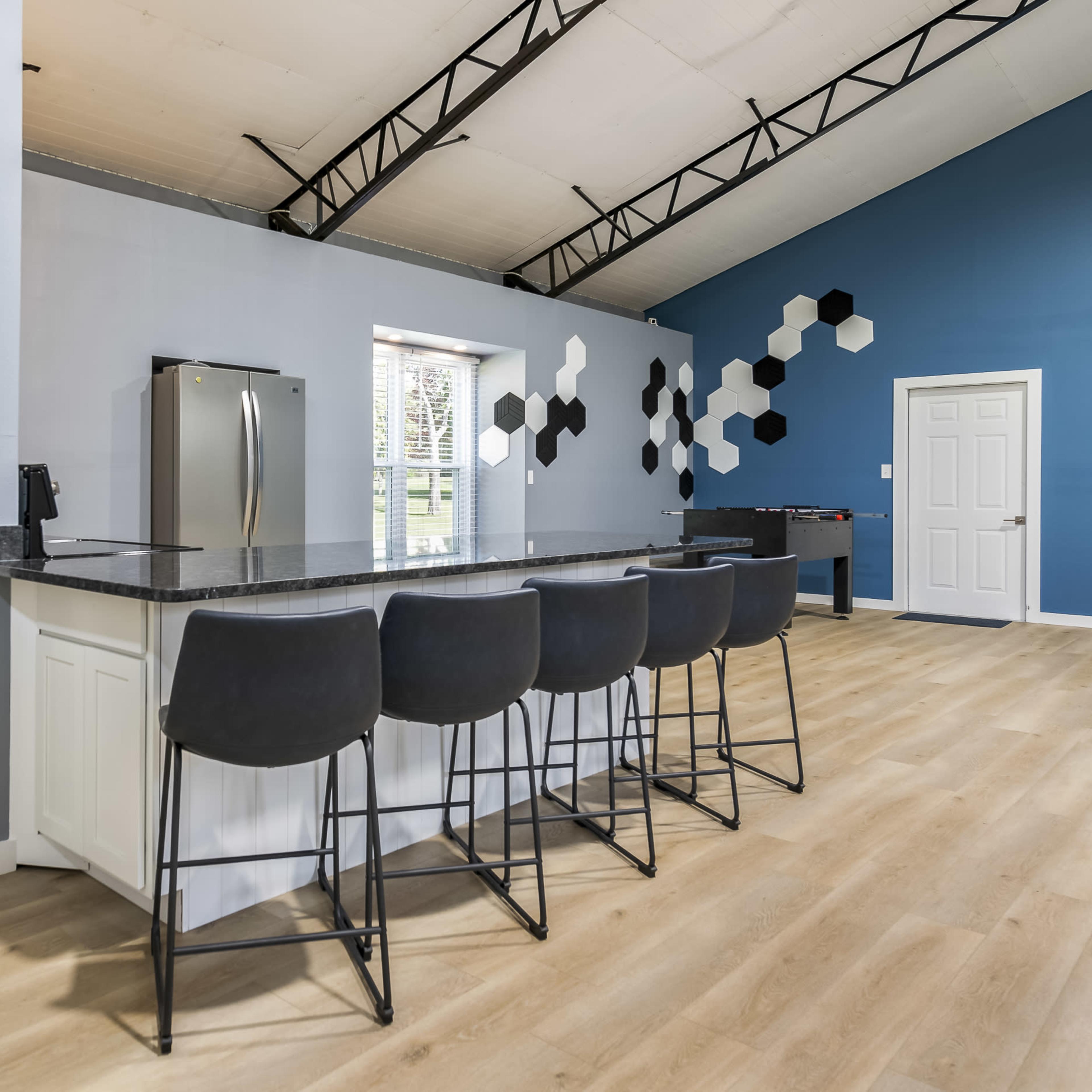 A modern kitchen area featuring a large island with bar stools, gray walls, and a connected bathroom visible to the left.