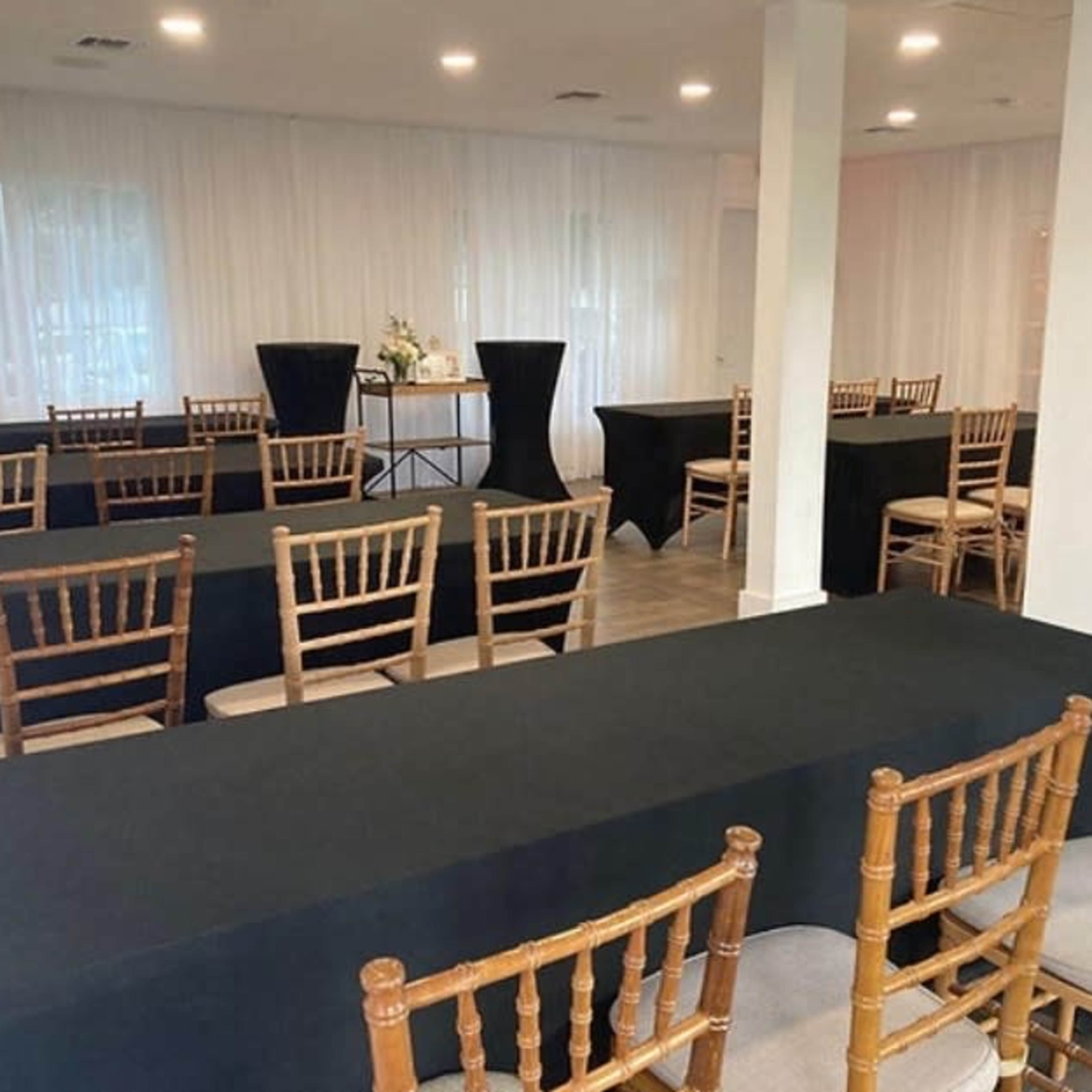 A banquet-style room with multiple rows of black tables and golden wooden chairs arranged for an event.