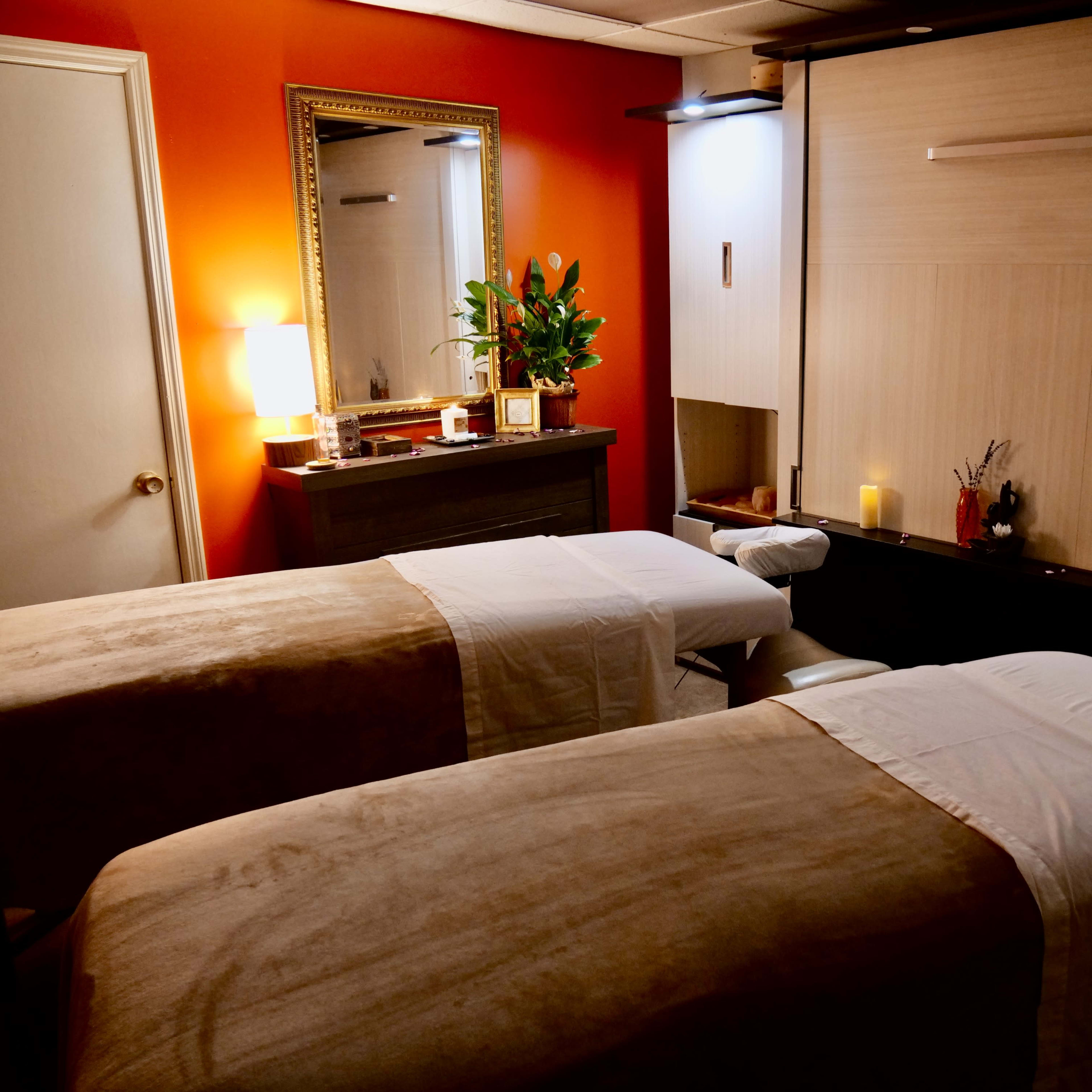A massage room with two massage tables, warm lighting, and a decorative mirror on the wall.