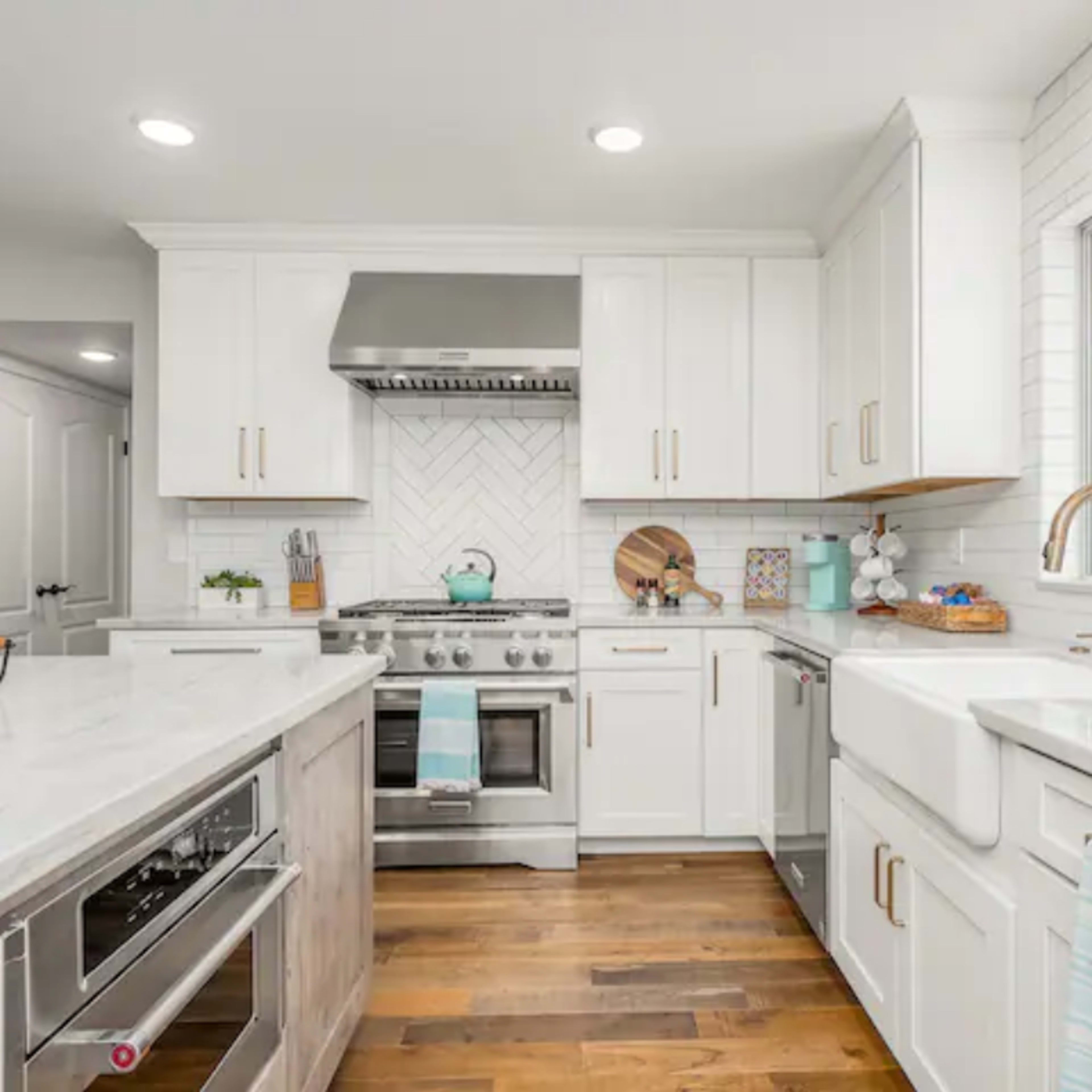 The kitchen features white cabinetry, stainless steel appliances, and a marble countertop with a farm sink and a large window.