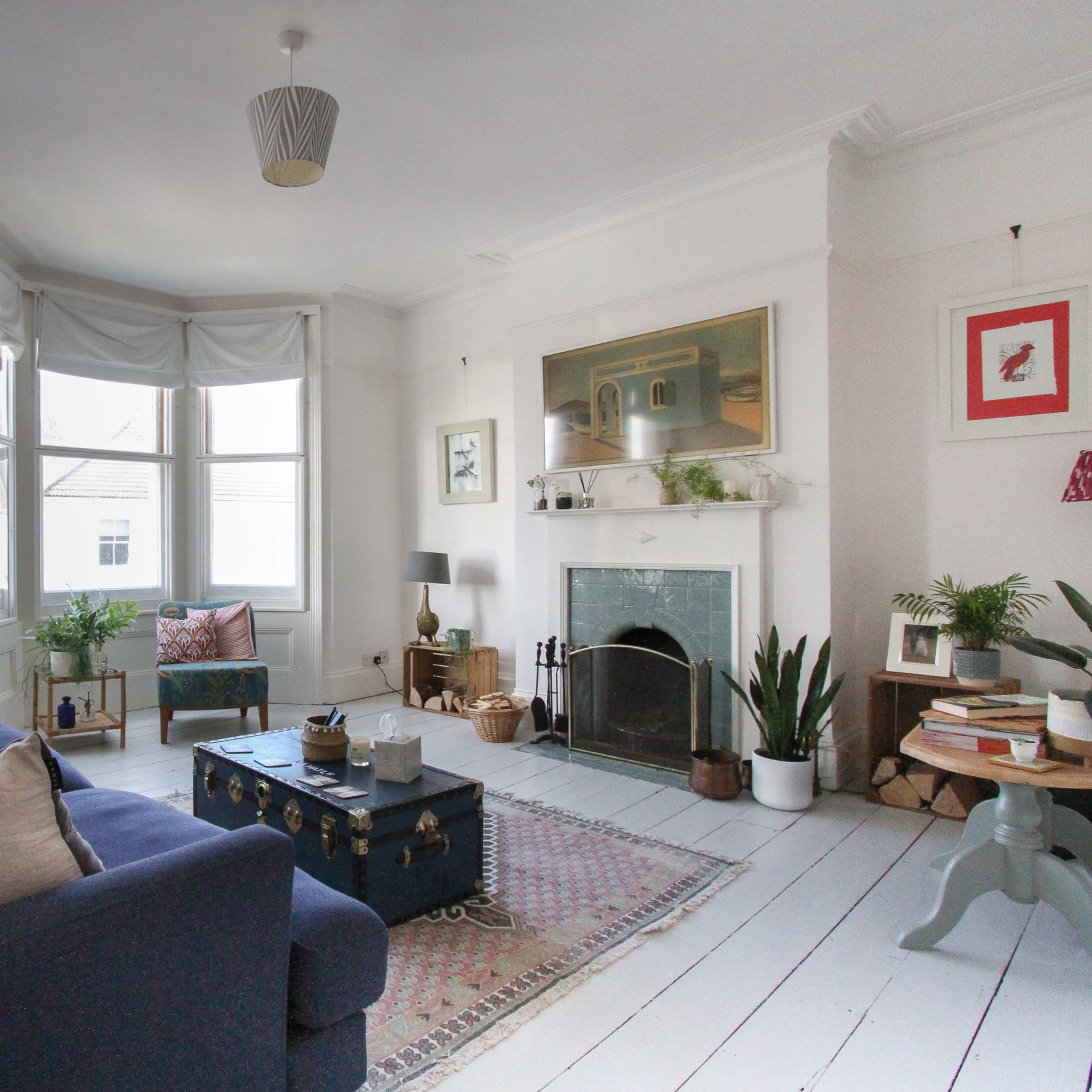 The living room features a blue sofa, a coffee table, and a fireplace, with large windows allowing natural light to fill the space.