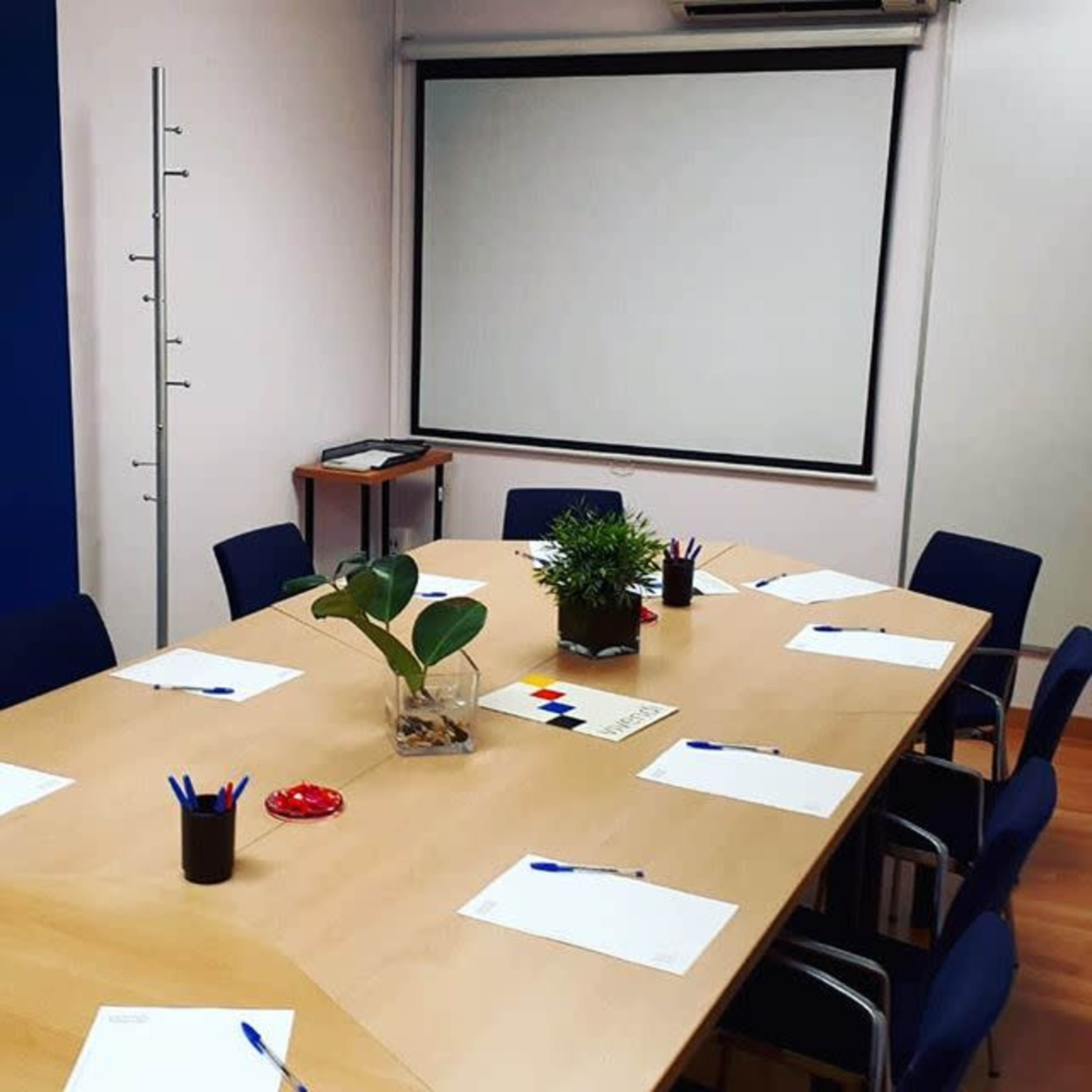 A conference room with a large table set for a meeting, featuring empty notepads, pens, and a potted plant.
