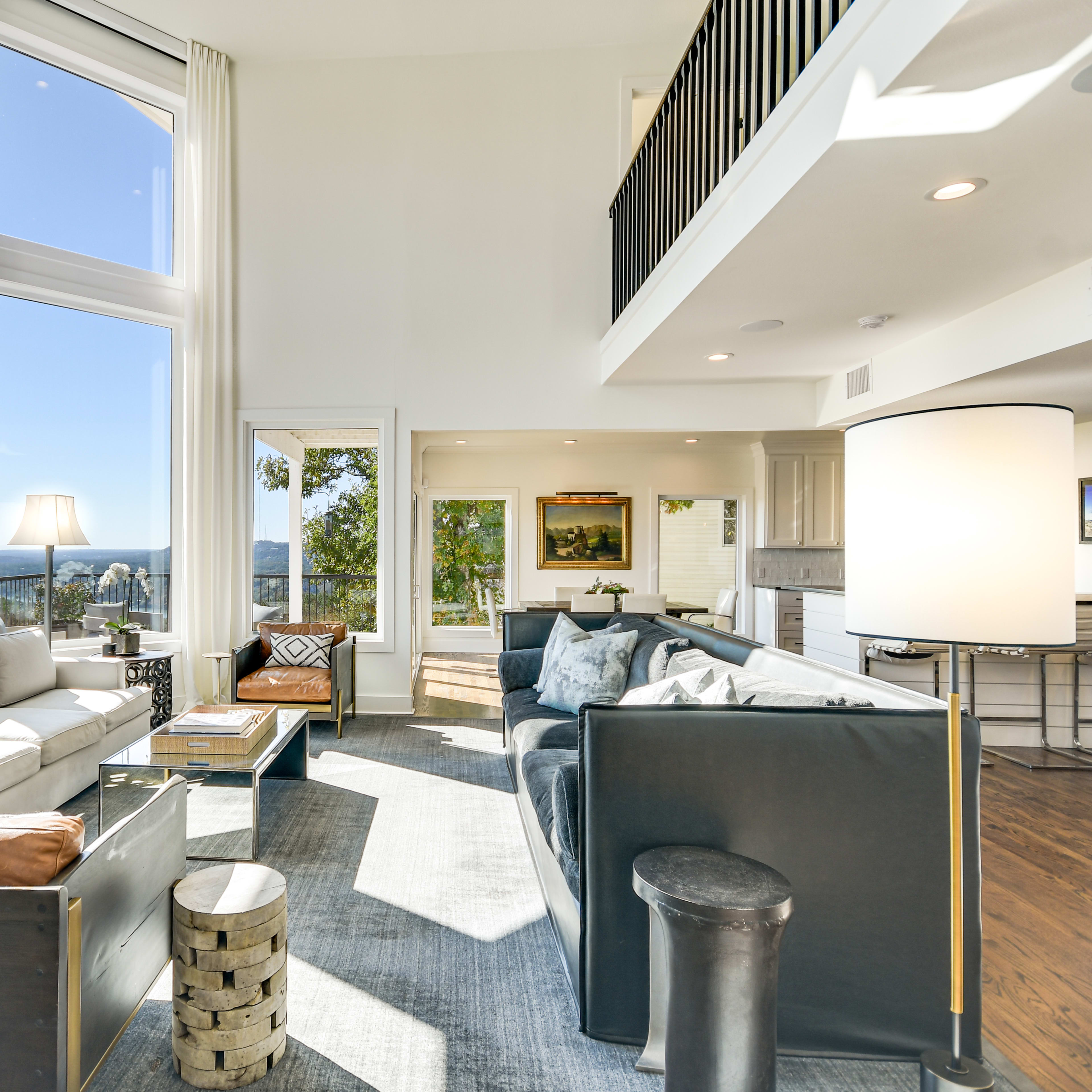 The room features large windows that allow for ample natural light, offering a view of the landscape beyond, with modern furniture arranged around a central area.