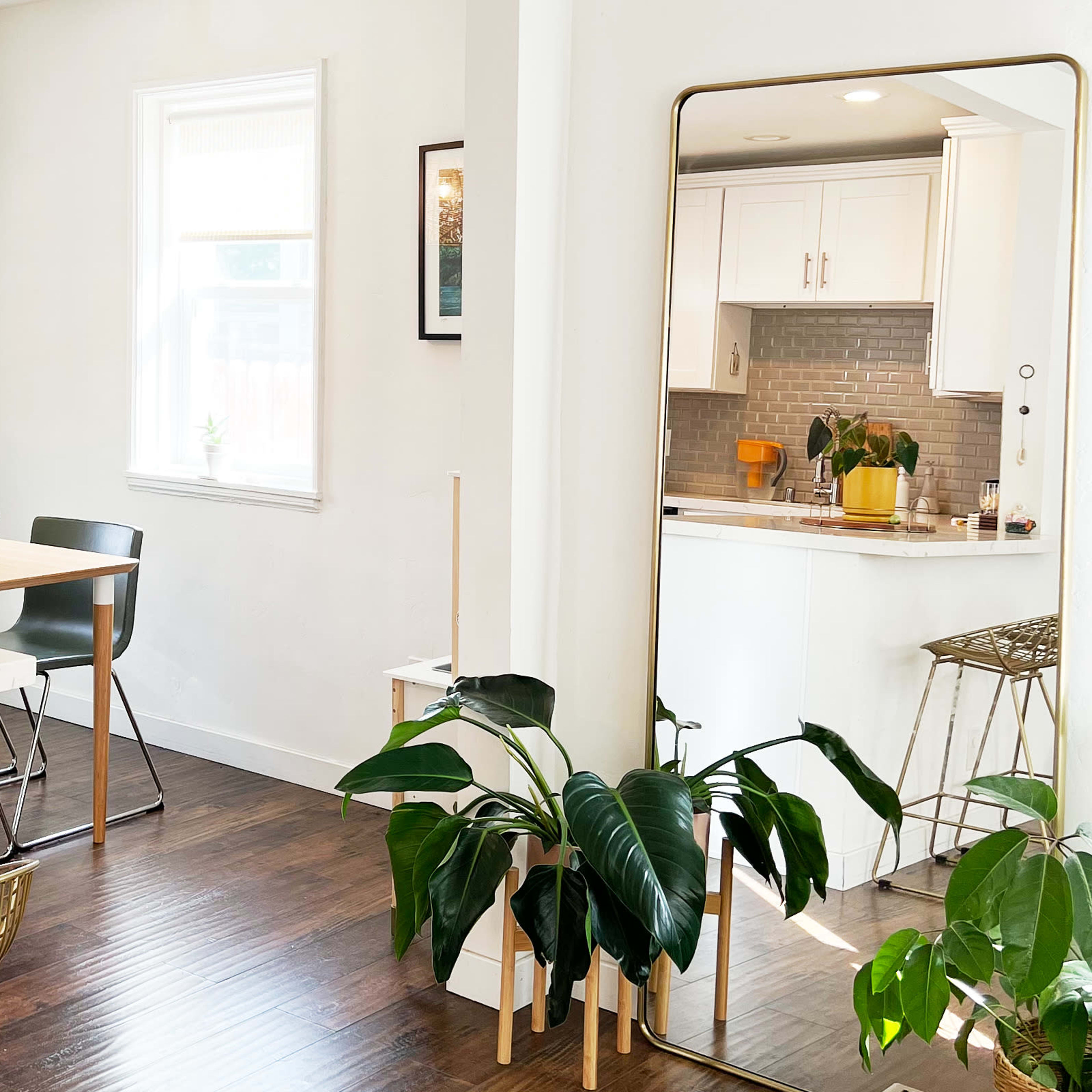 A modern kitchen and dining area featuring a wooden table with black chairs, a large mirror, and various houseplants.