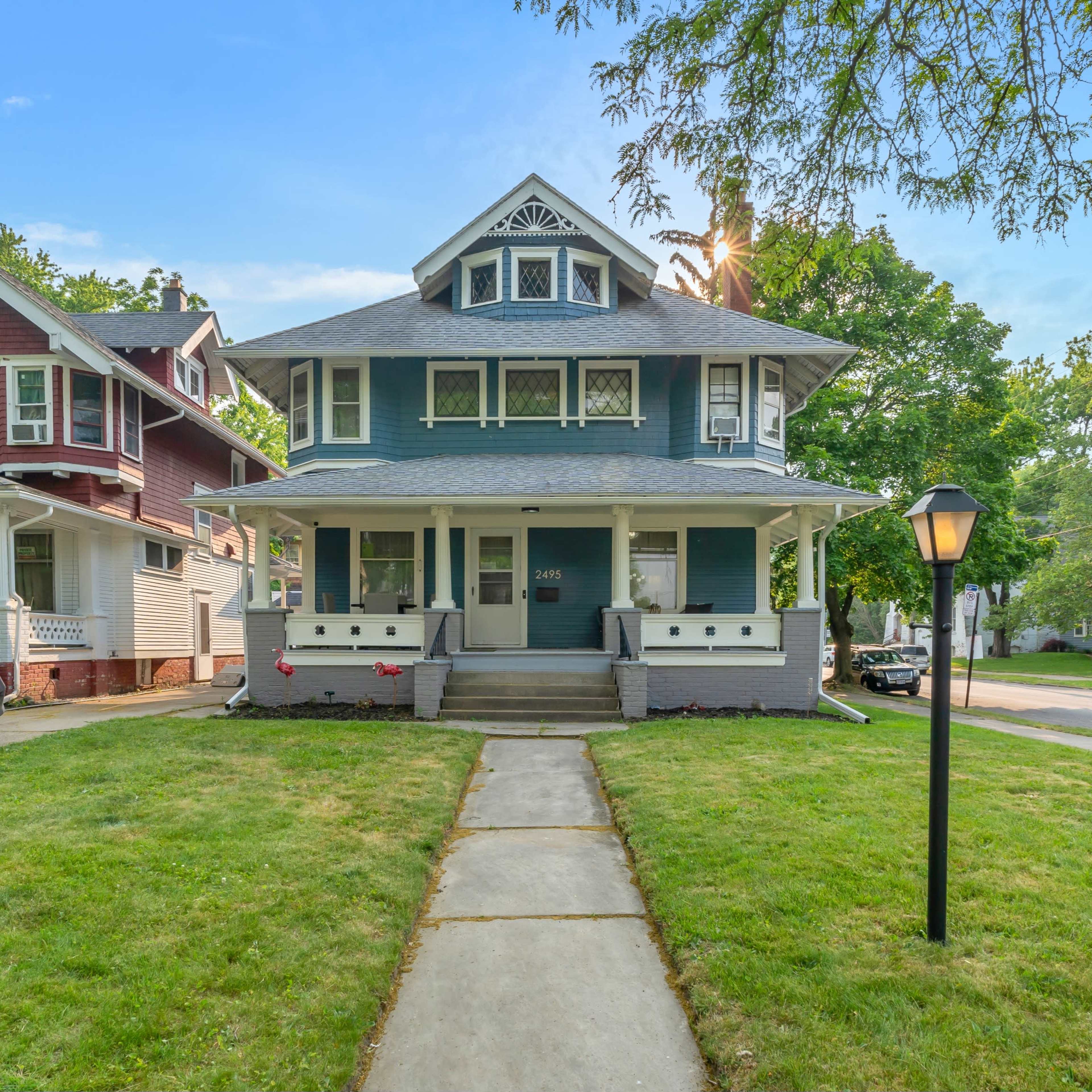 A two-story blue house with a steeply pitched roof, a front porch, and a manicured lawn.