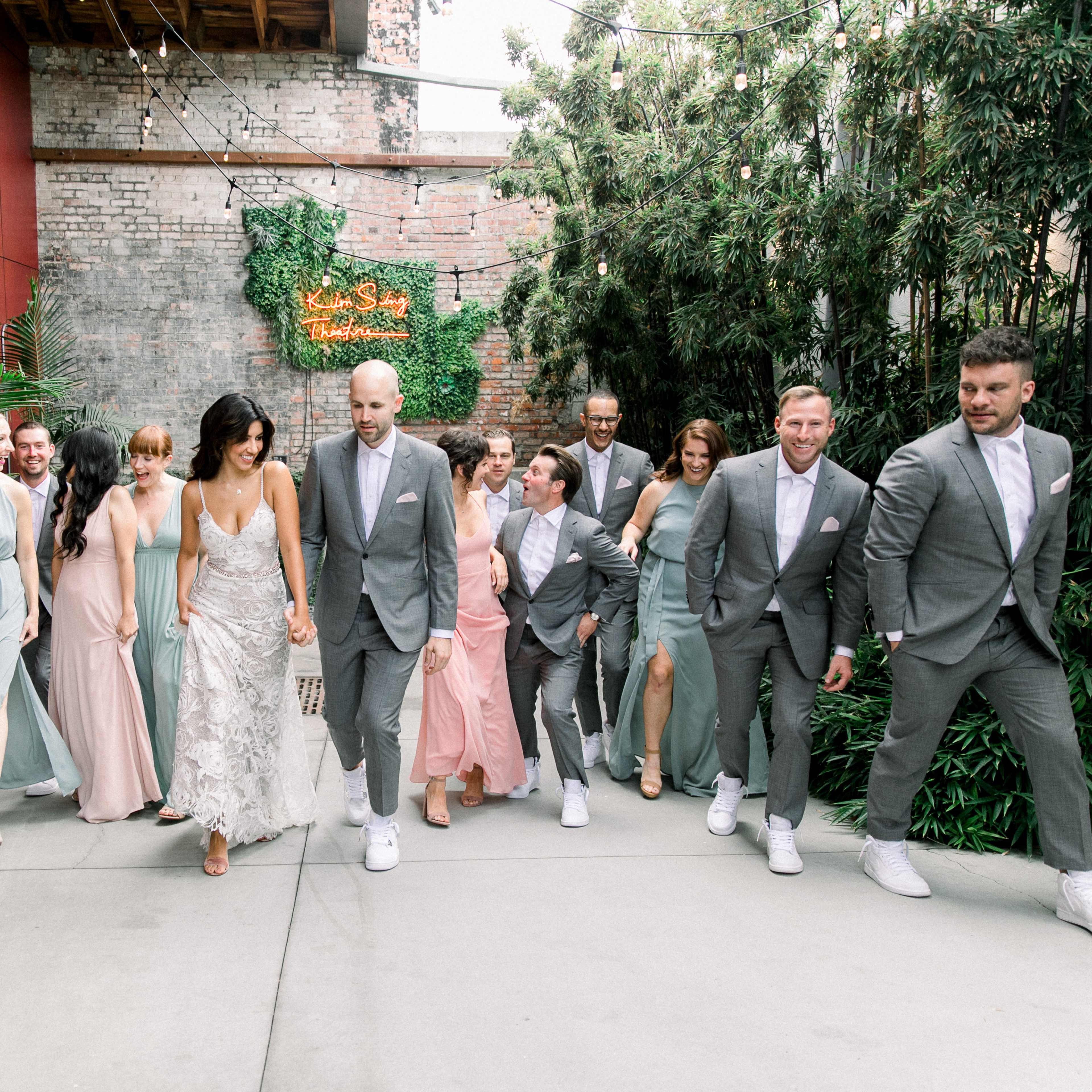A wedding party wearing formal attire walks together in a bright outdoor setting.