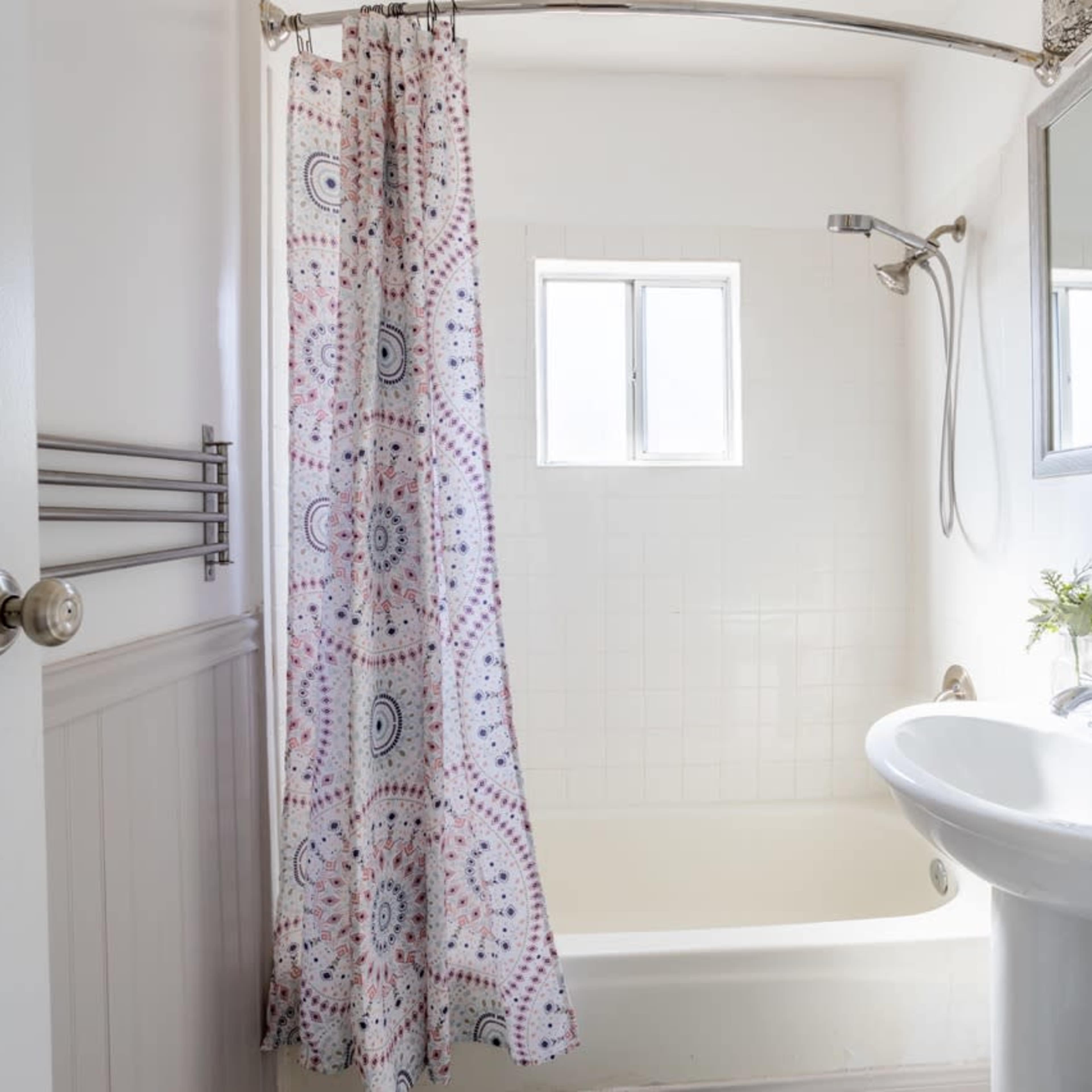 A bathroom with a bathtub, a showerhead, a white sink, and a patterned shower curtain.