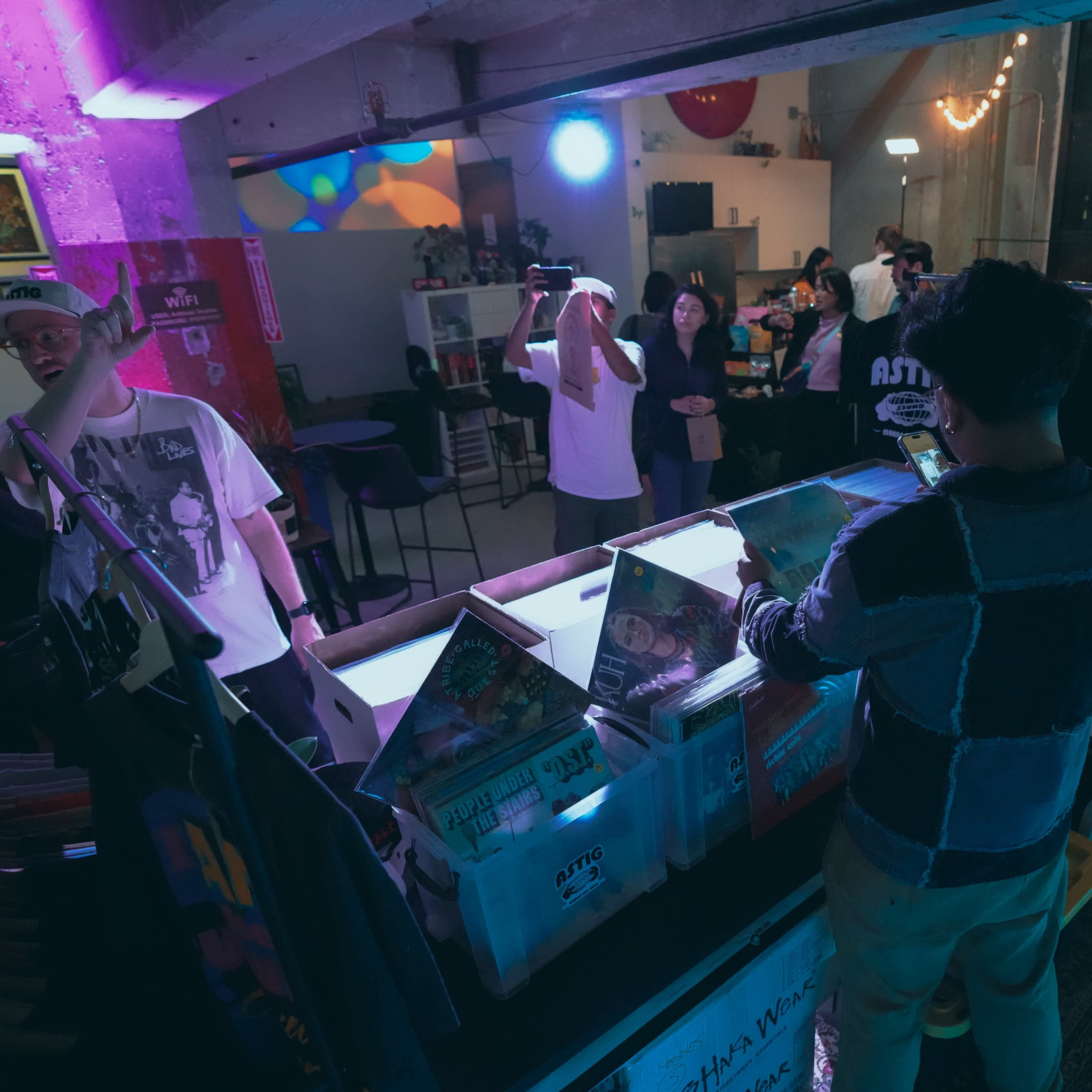 A group of people socialize at a vibrant indoor event space while one person browses through a collection of vinyl records.
