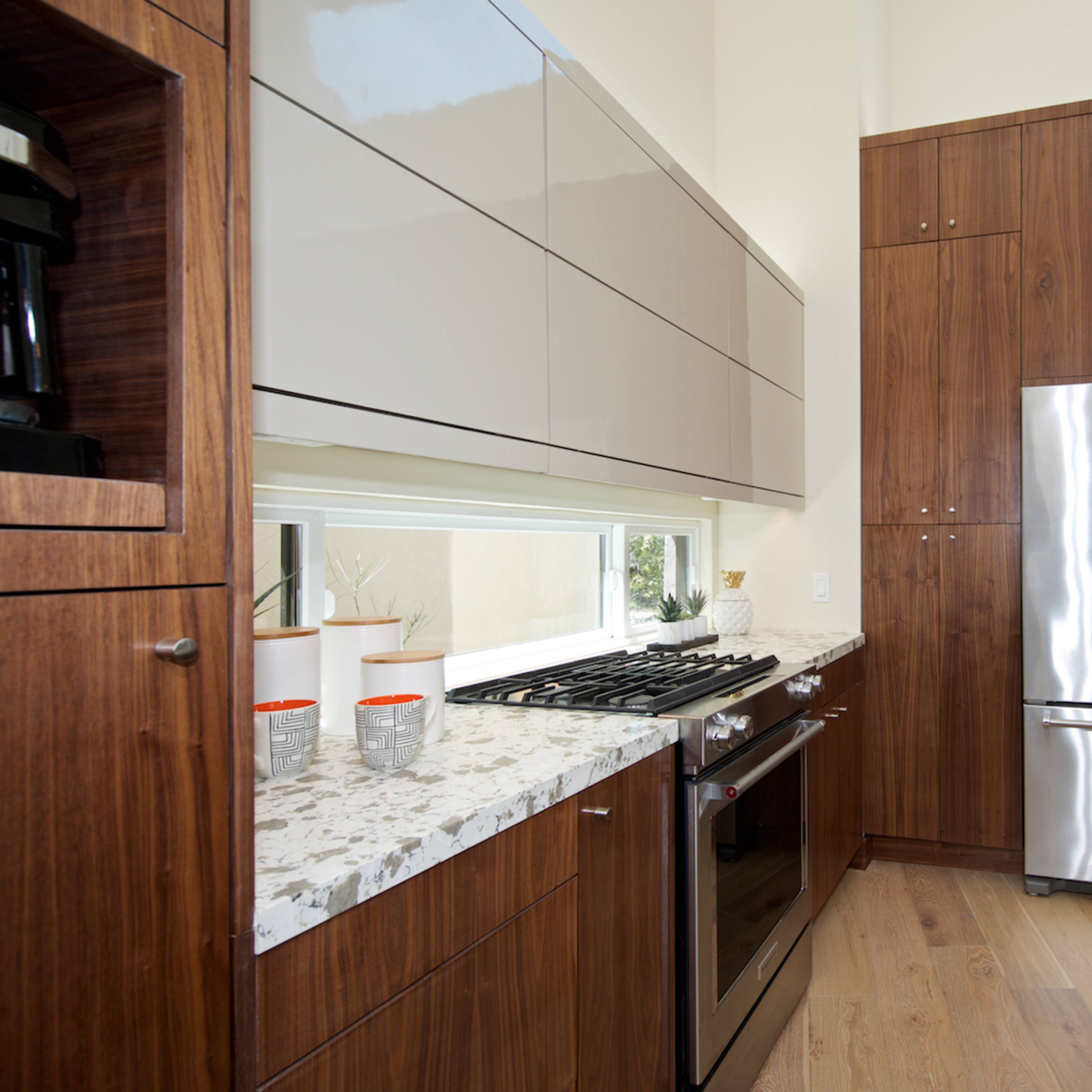 A modern kitchen with wooden cabinets, a stainless steel refrigerator, and a gas stove with a marble countertop.