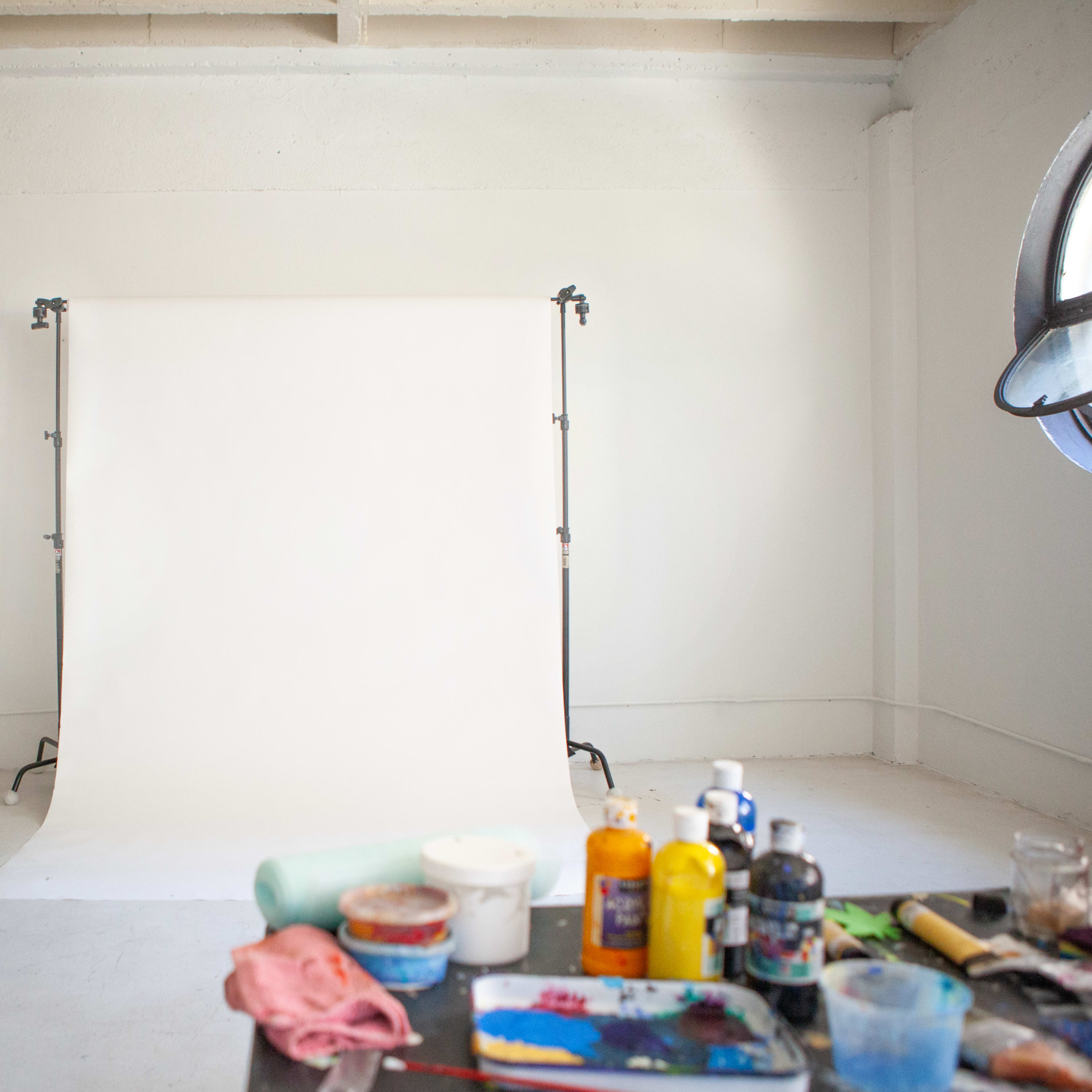 A well-lit studio space with a blank white backdrop, a chair, and art supplies scattered on a table.