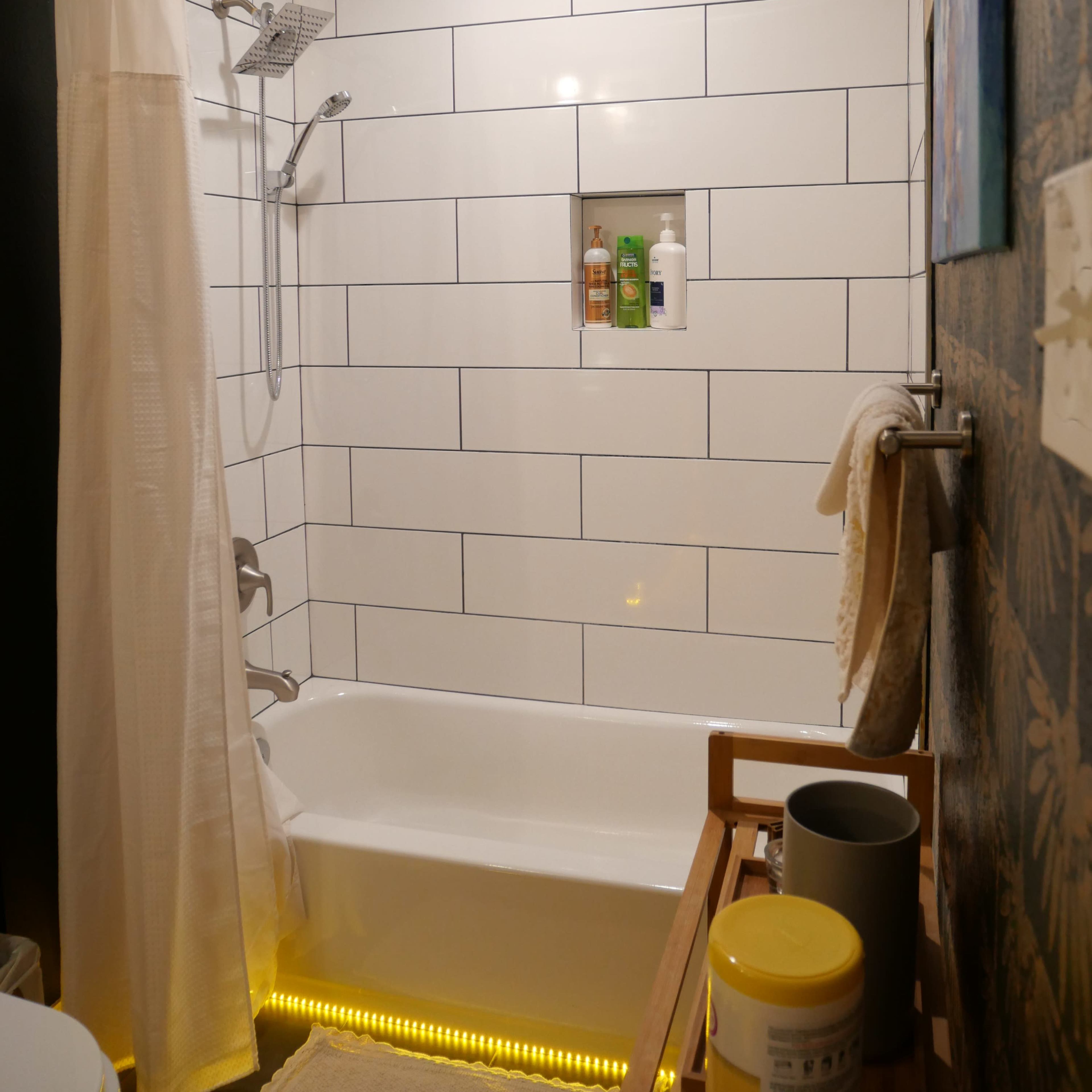 A clean bathroom features a shower with a glass door, a bathtub, and a tiled wall with a built-in shelf displaying toiletries.