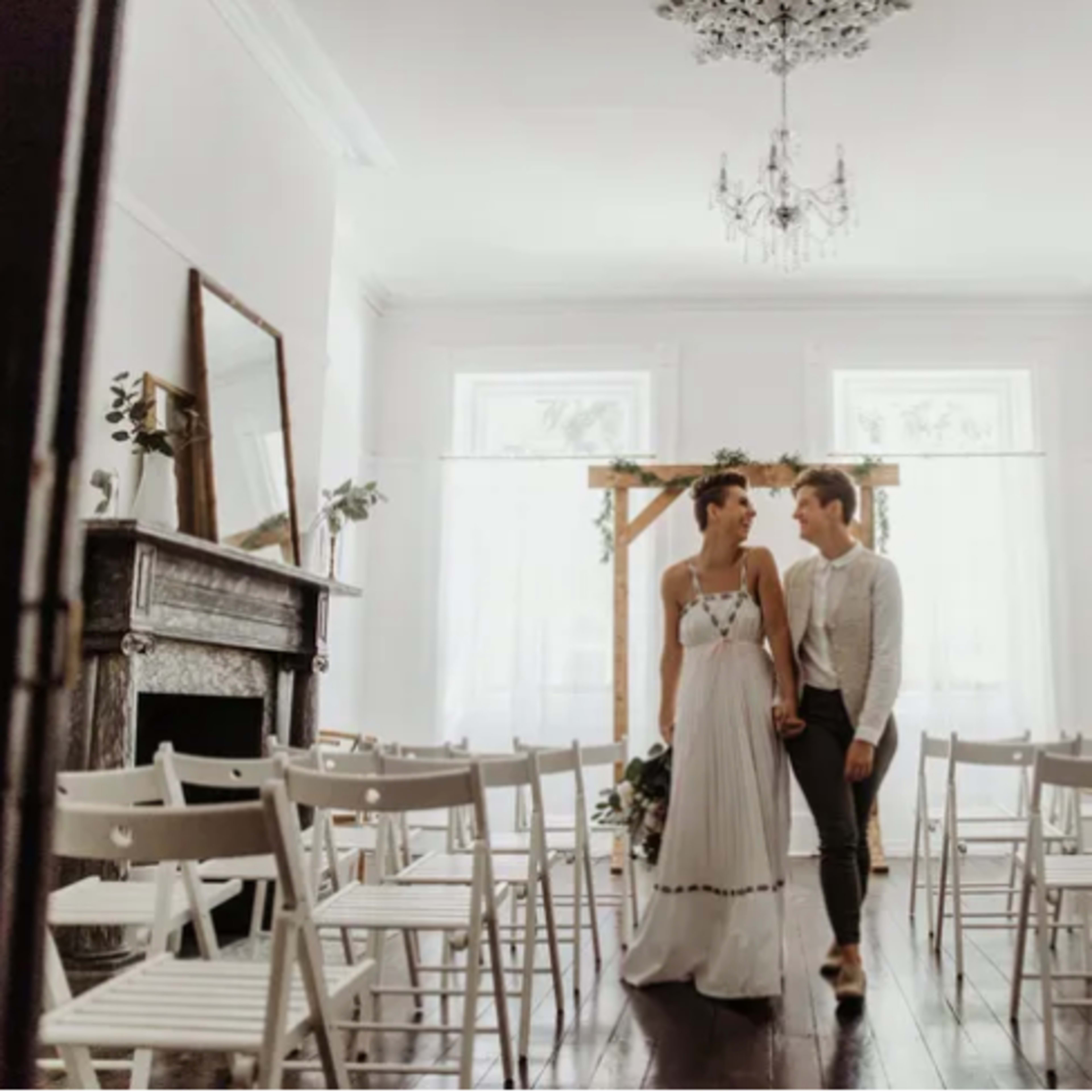 A bride and groom walk hand in hand down the aisle of a lightly decorated indoor venue set up for a wedding ceremony.