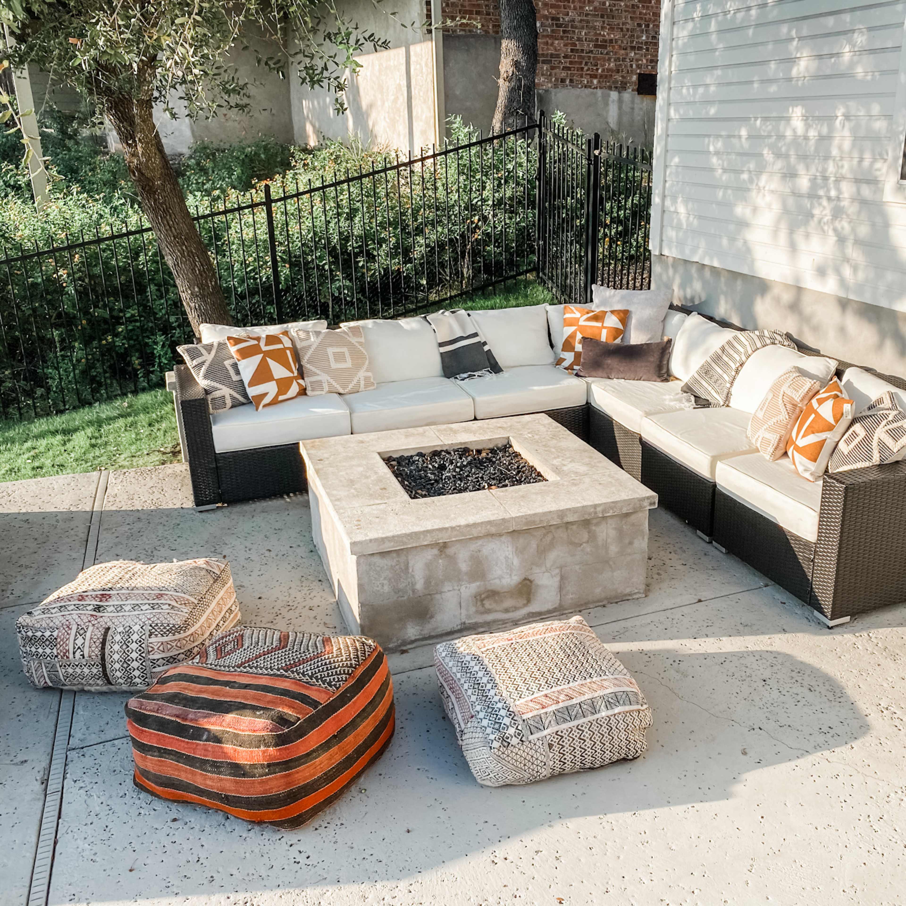 A patio area features a sectional sofa with decorative cushions and a rectangular fire pit surrounded by additional seating cushions.