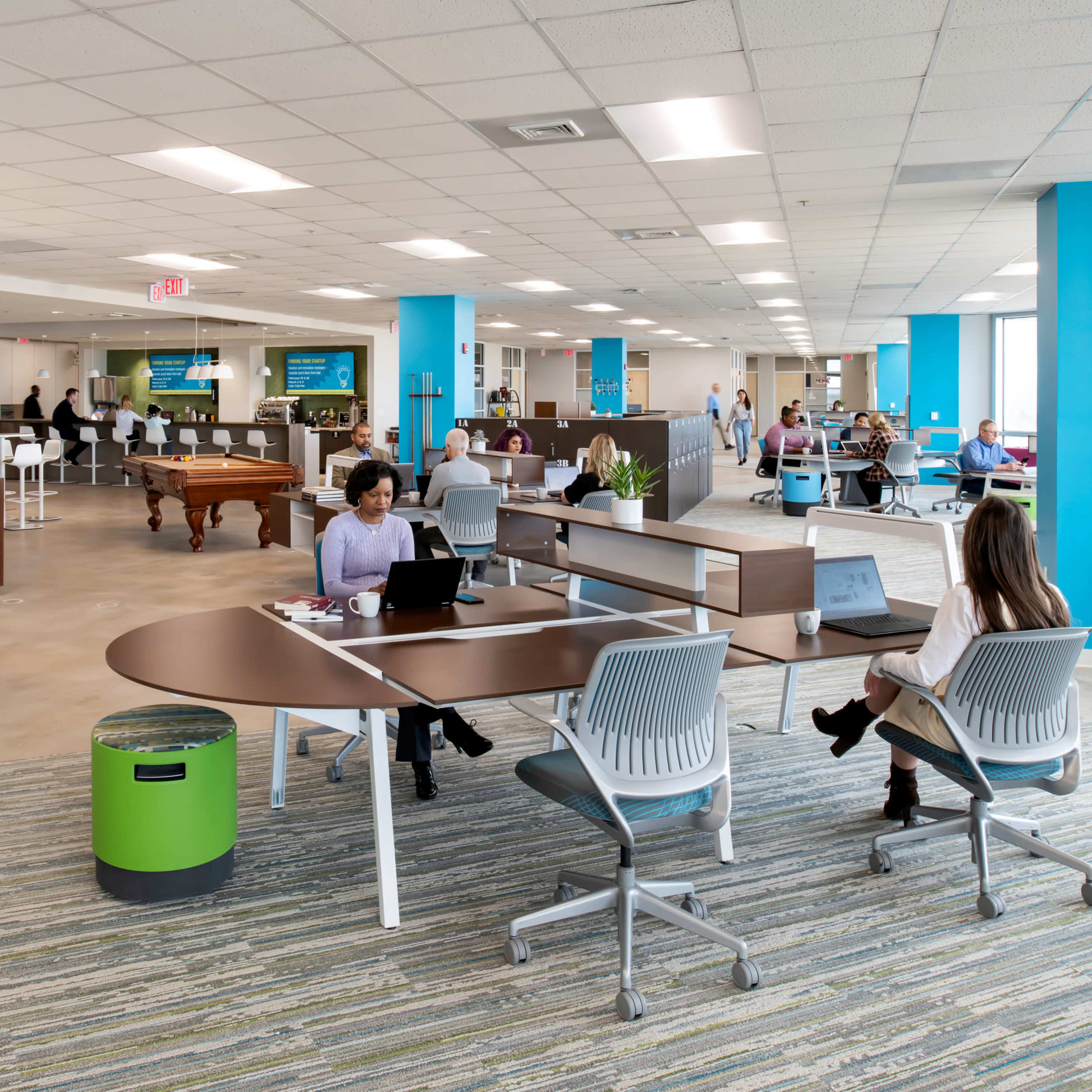 A modern office space featuring a mix of workstations, a lounge area with a pool table, and employees engaging in various activities throughout the room.