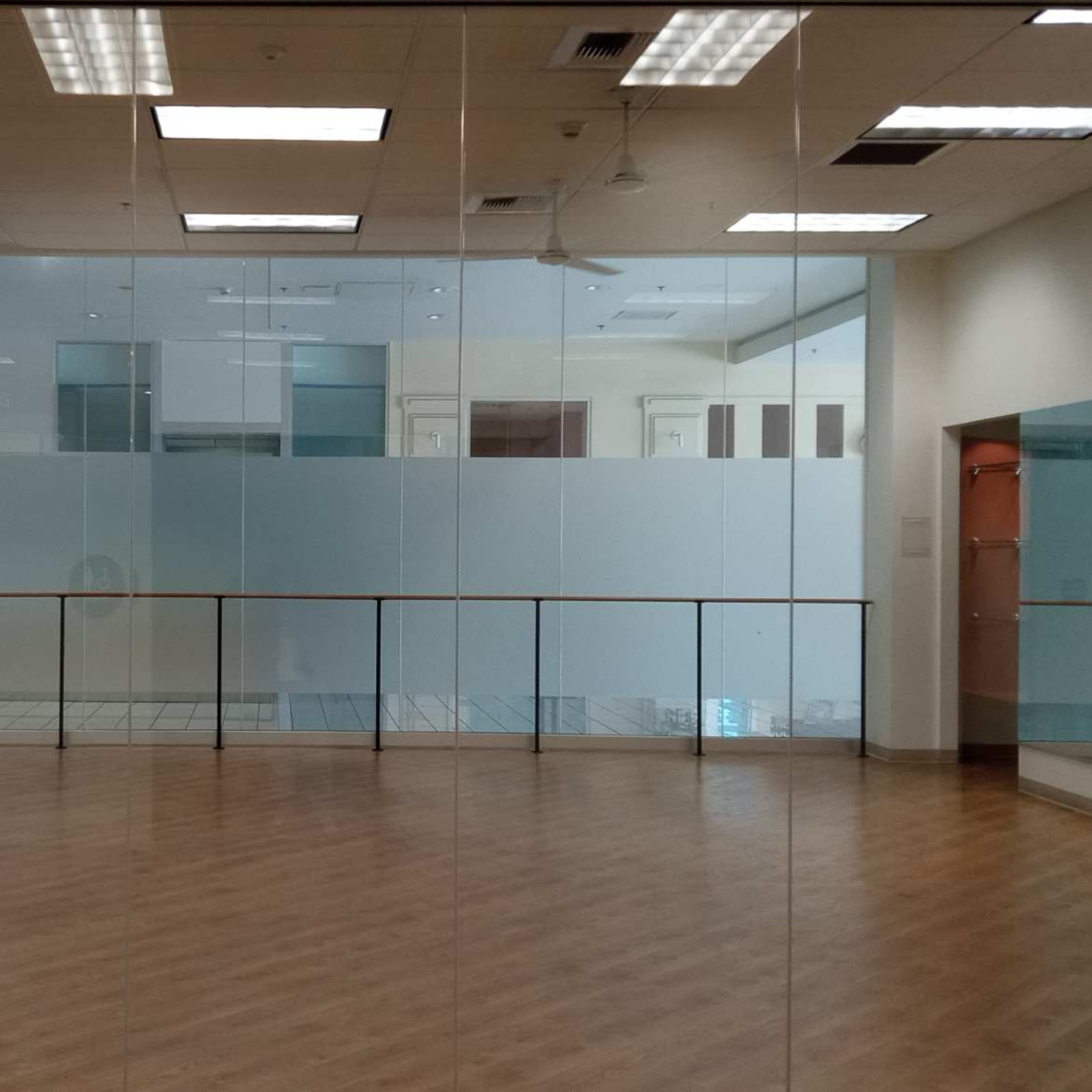 A spacious, empty room with a wooden floor and mirrored walls.