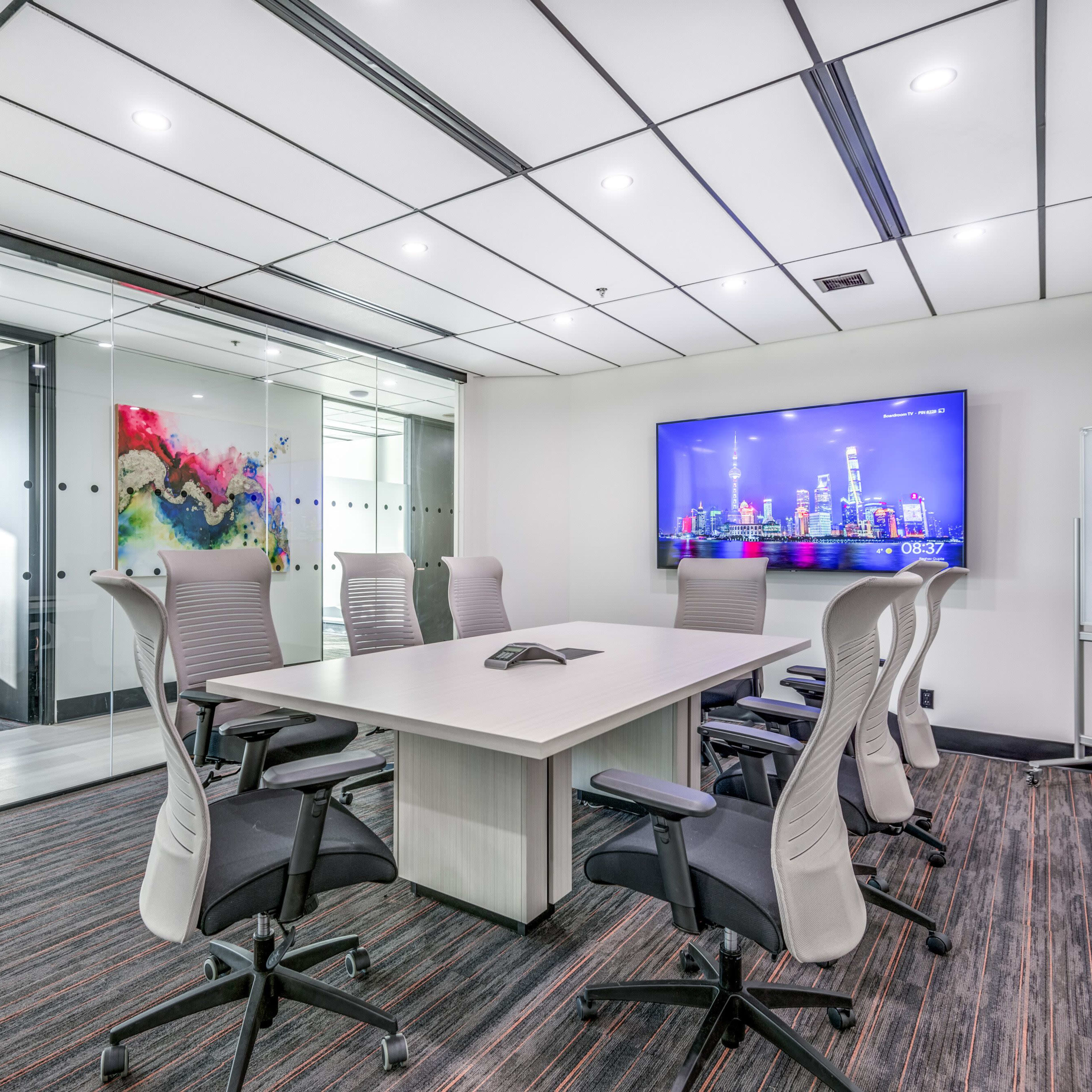 A modern conference room features a large table surrounded by ergonomic chairs, with a wall-mounted screen displaying a city skyline.