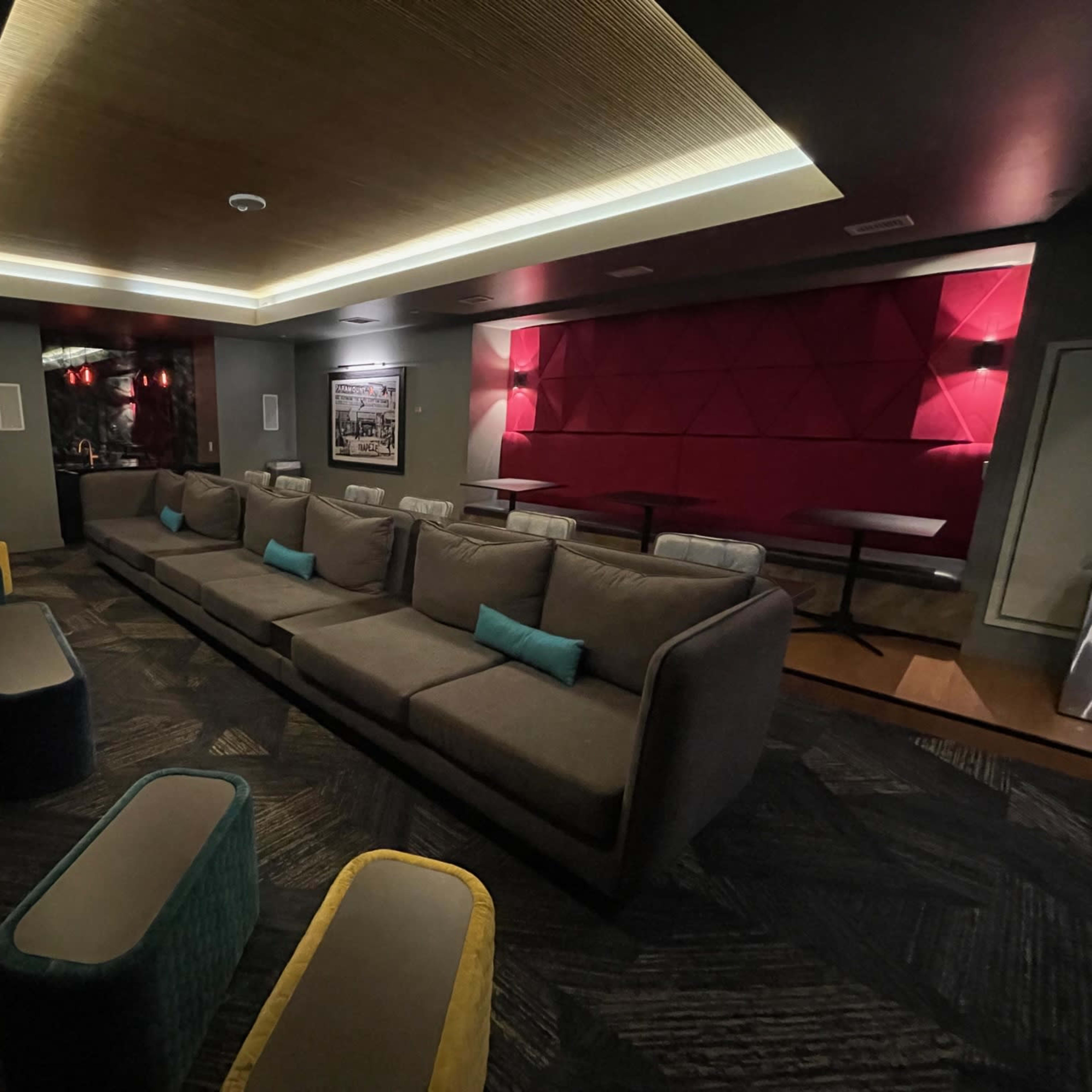 A modern lounge area with a large gray sectional sofa and colorful stools under soft lighting.