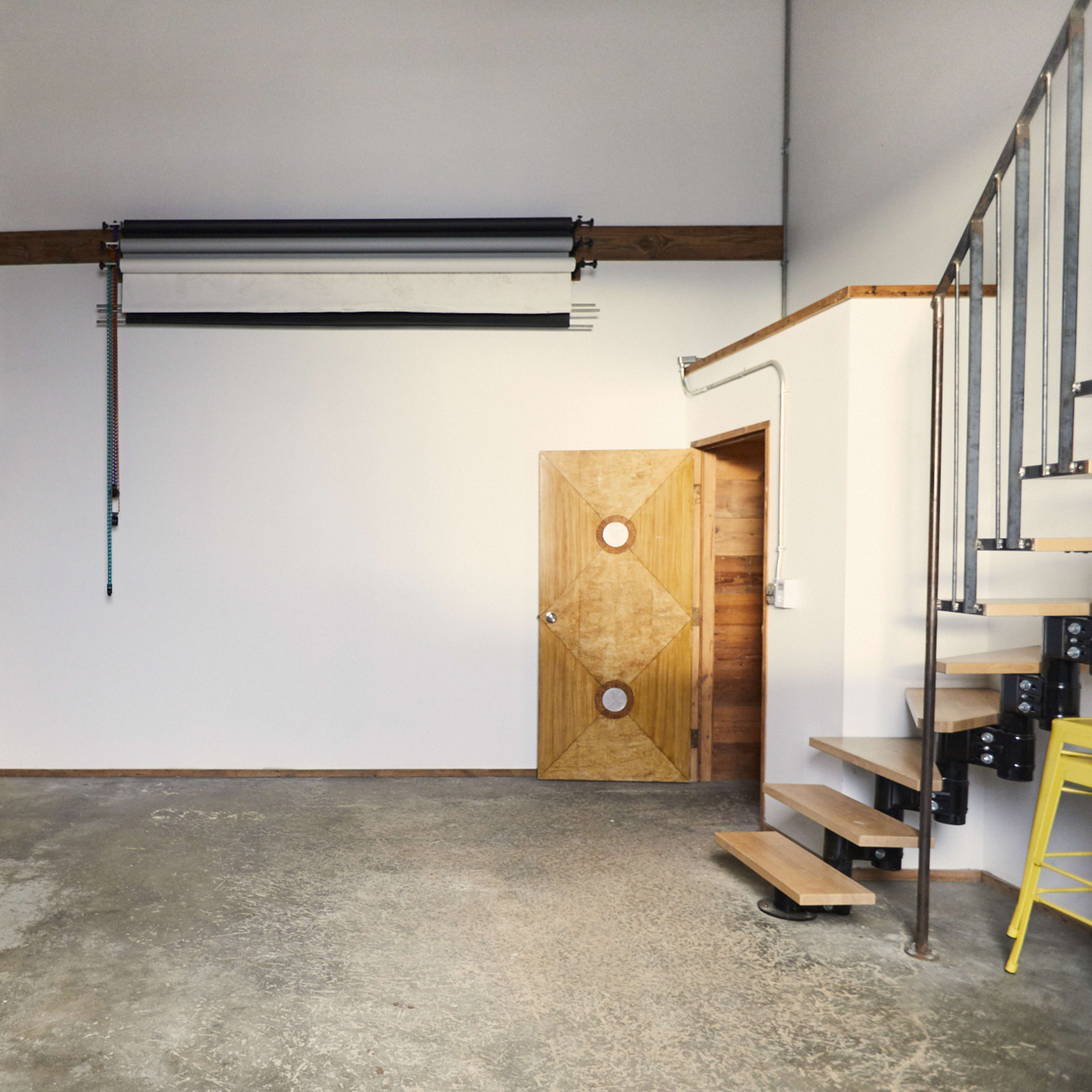 An interior space with a wooden wall, a white wall, a staircase, and a door featuring circular handles.
