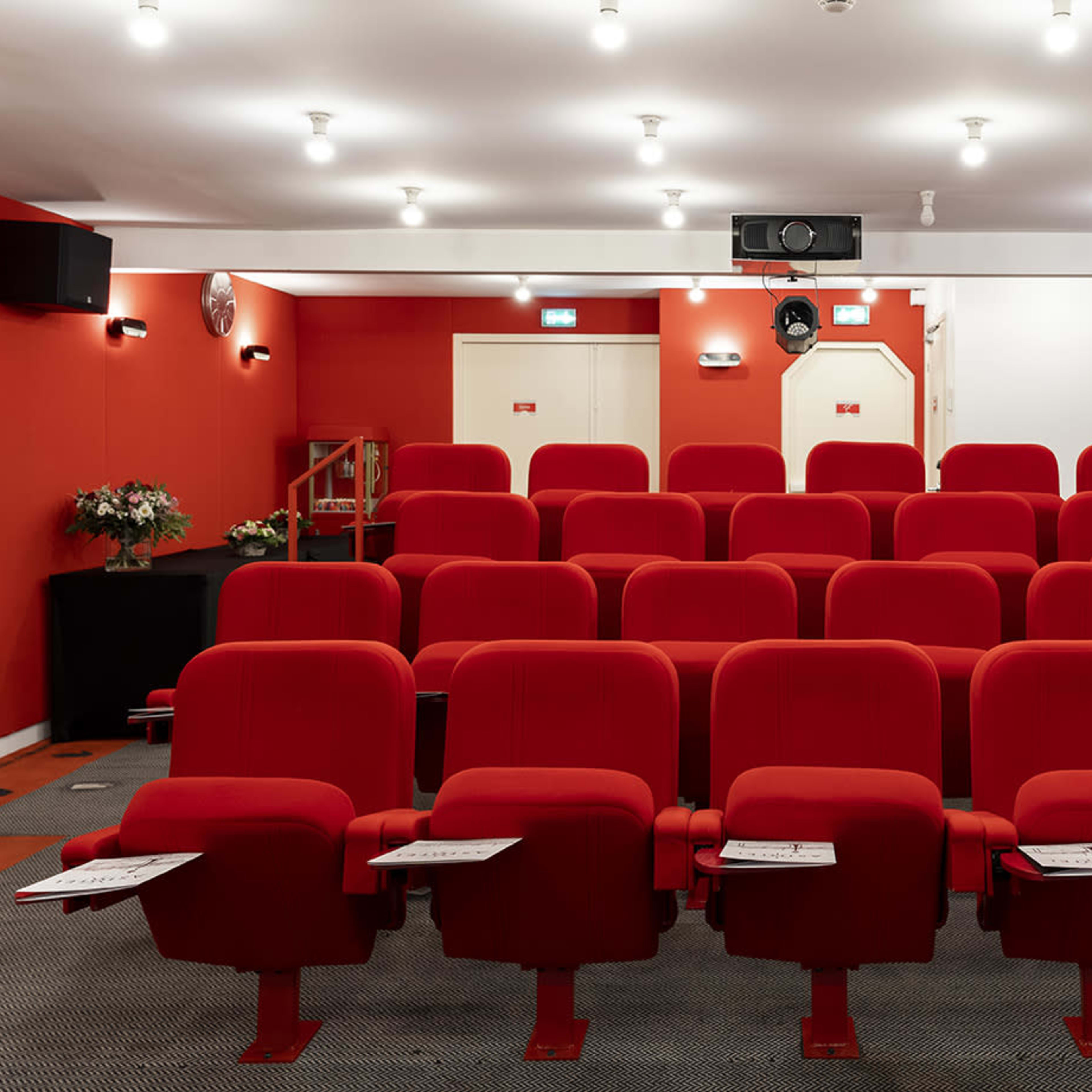 A small auditorium with rows of red seating and a projector mounted on the ceiling.