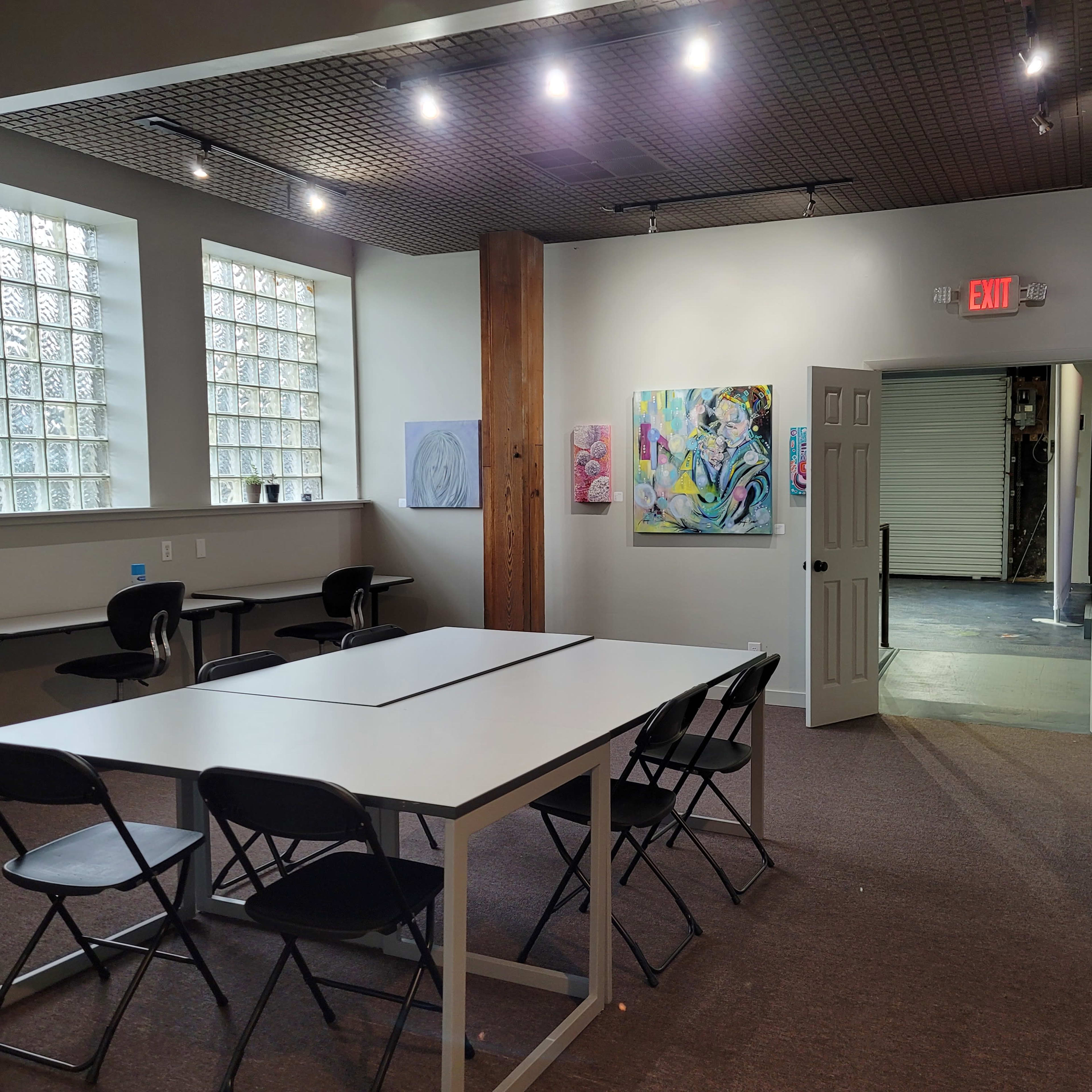A spacious room with a long table surrounded by black chairs, decorated with artwork on the walls and a doorway leading to another area.