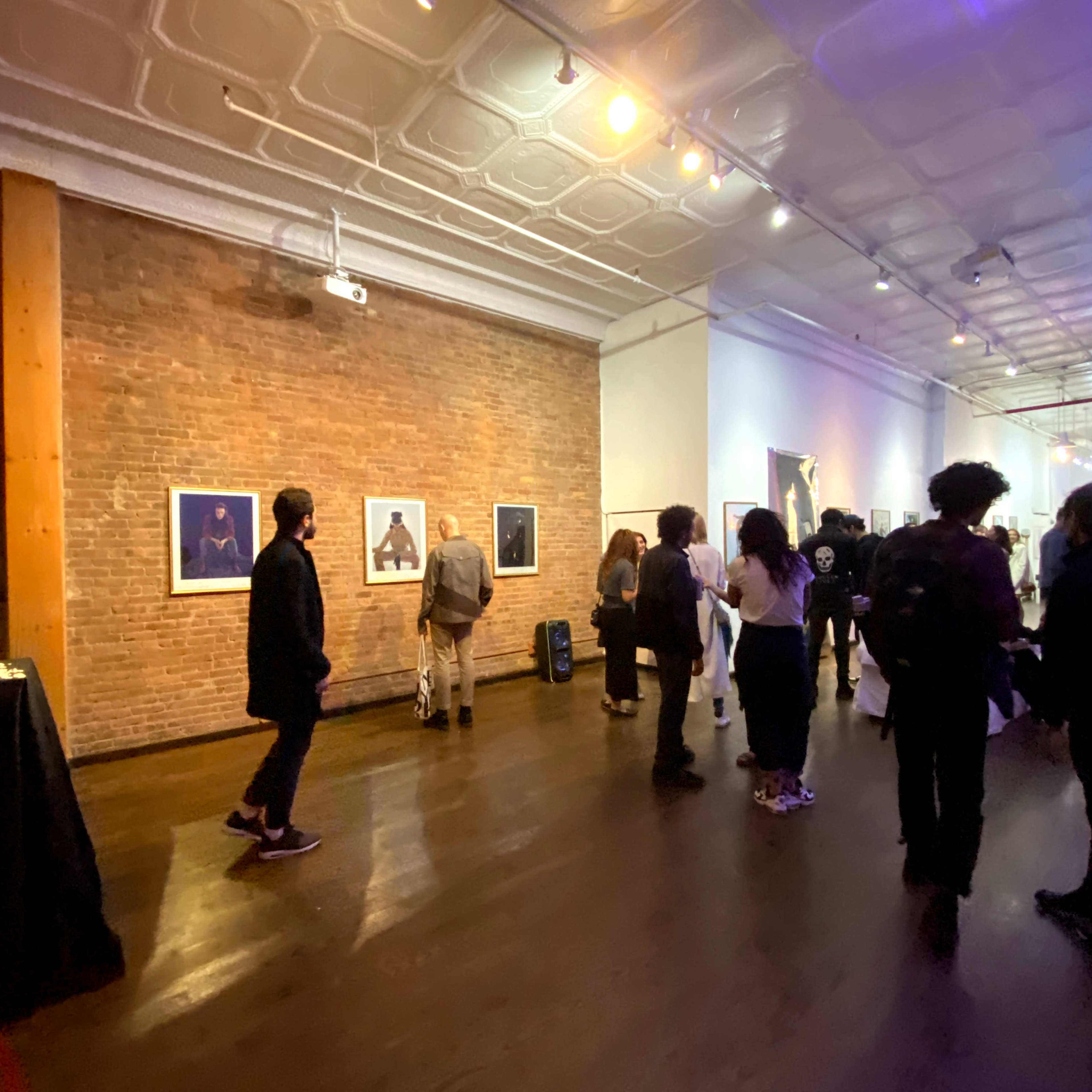People are viewing artwork in an art gallery with exposed brick walls and a wooden floor.