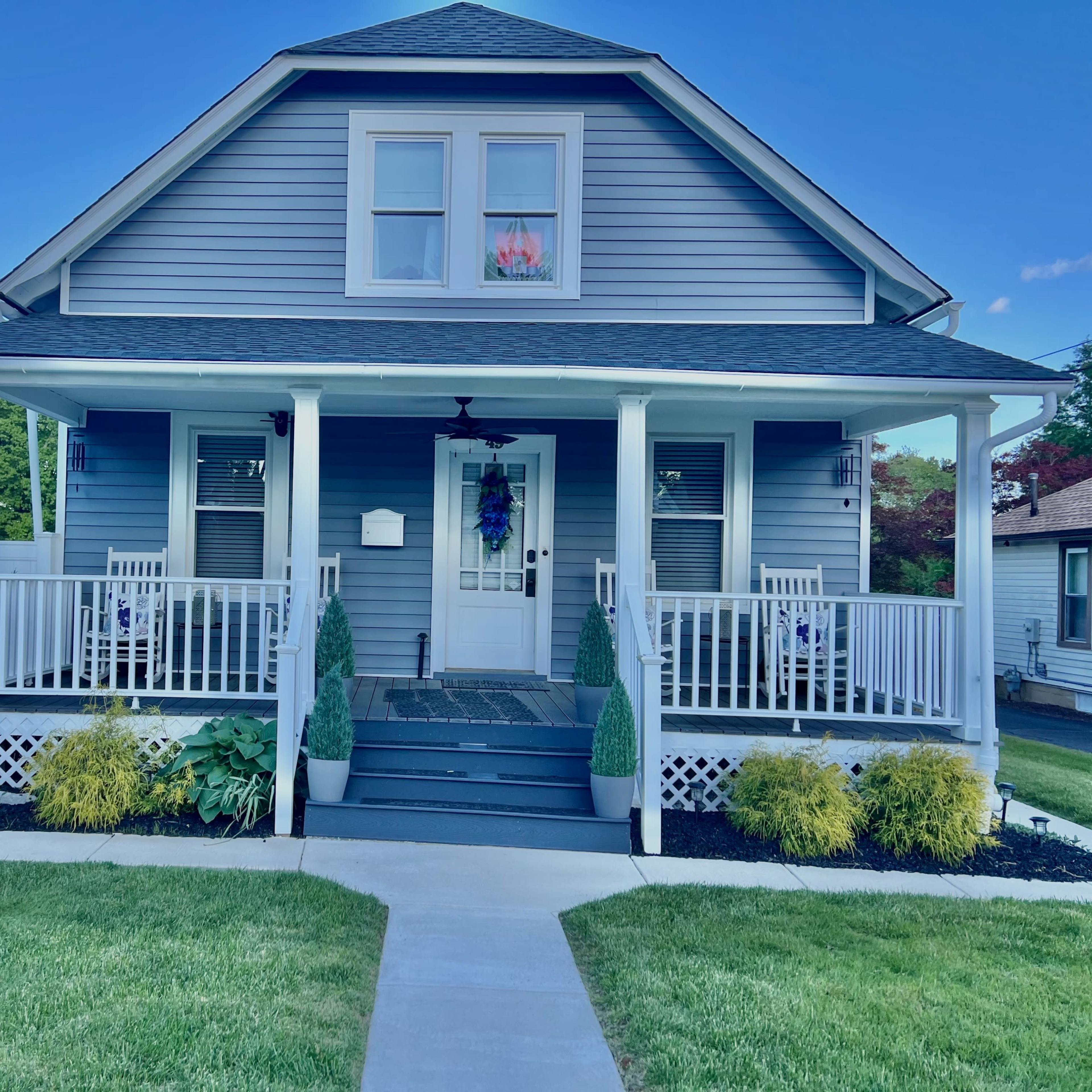 A two-story blue house with white trim, a front porch supported by decorative columns, and a neatly landscaped yard.