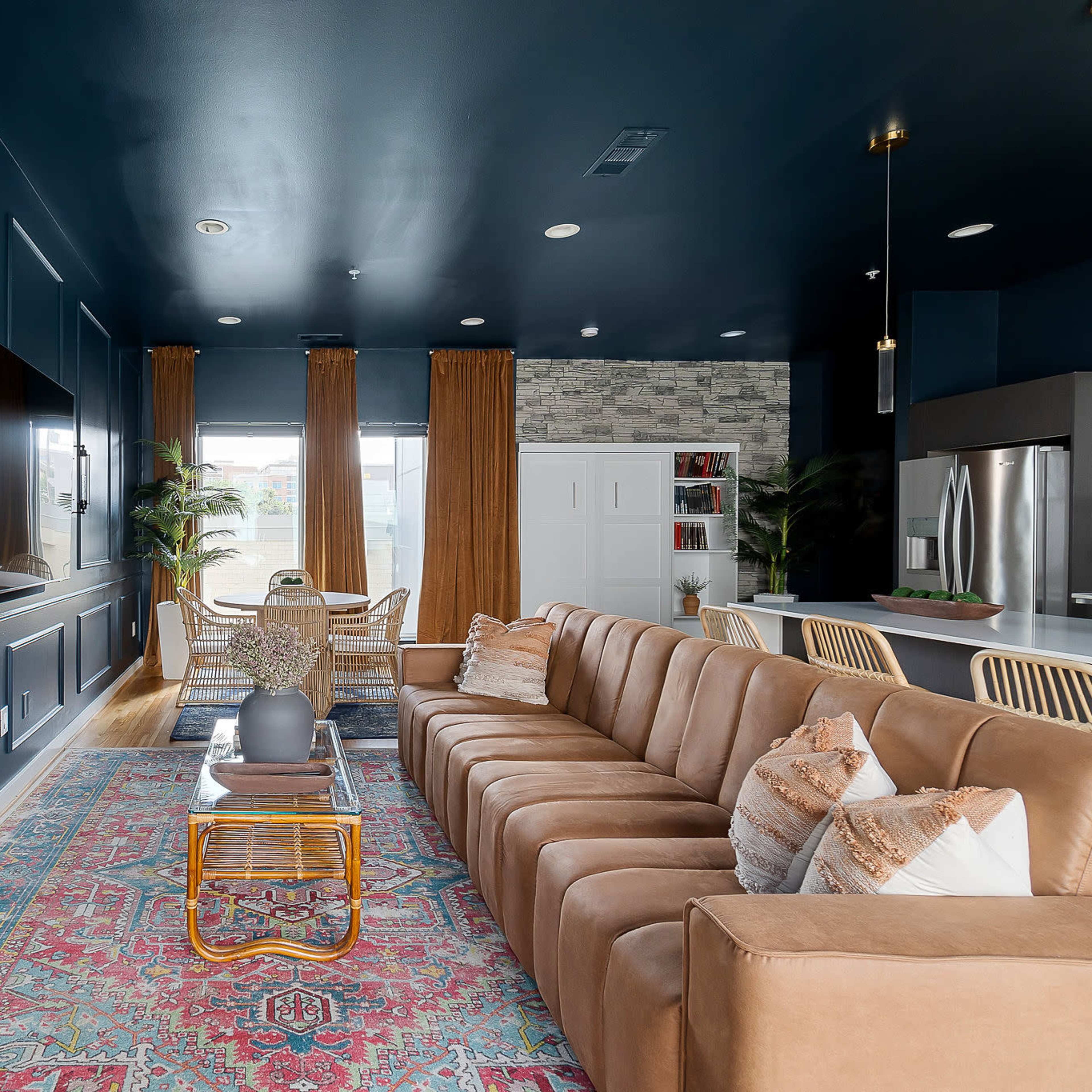 A modern living room features a large brown sectional sofa, a flat-screen TV mounted on a navy blue wall, and a dining area visible in the background.
