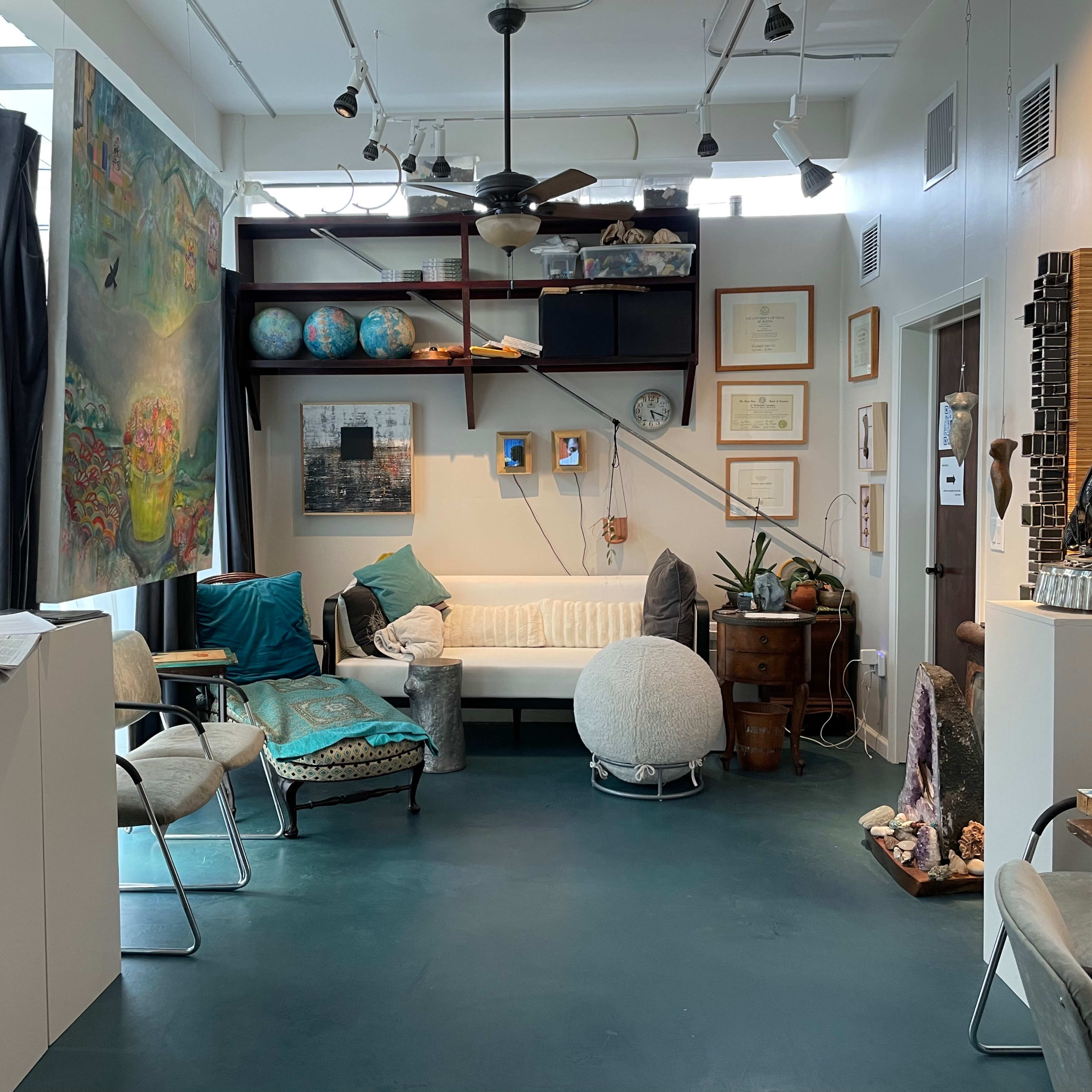 A cozy studio or office space featuring various seating options, artwork on the walls, and decorative globes on a bookshelf.