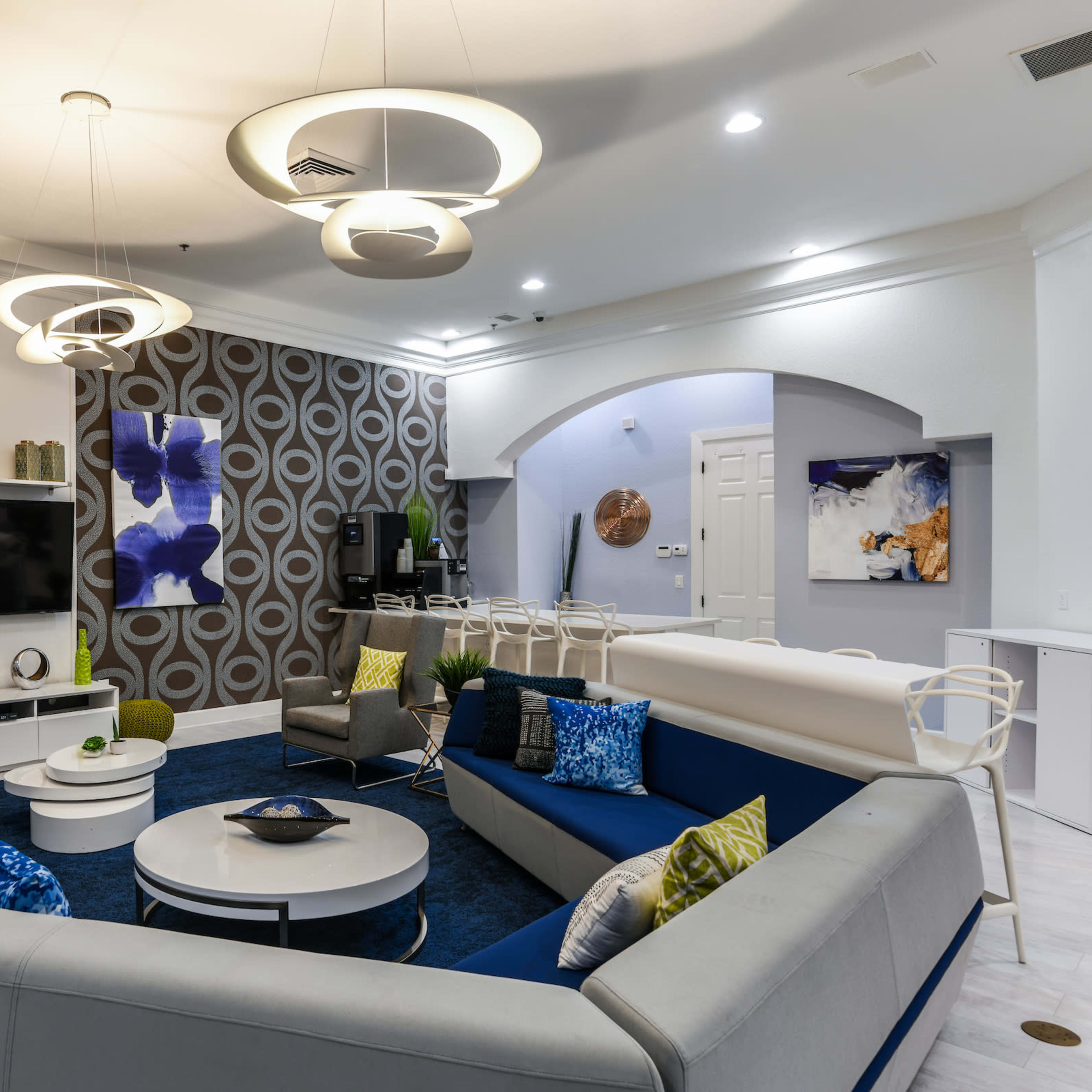 A modern, stylish living area featuring a round sofa, circular light fixtures, and abstract wall art.