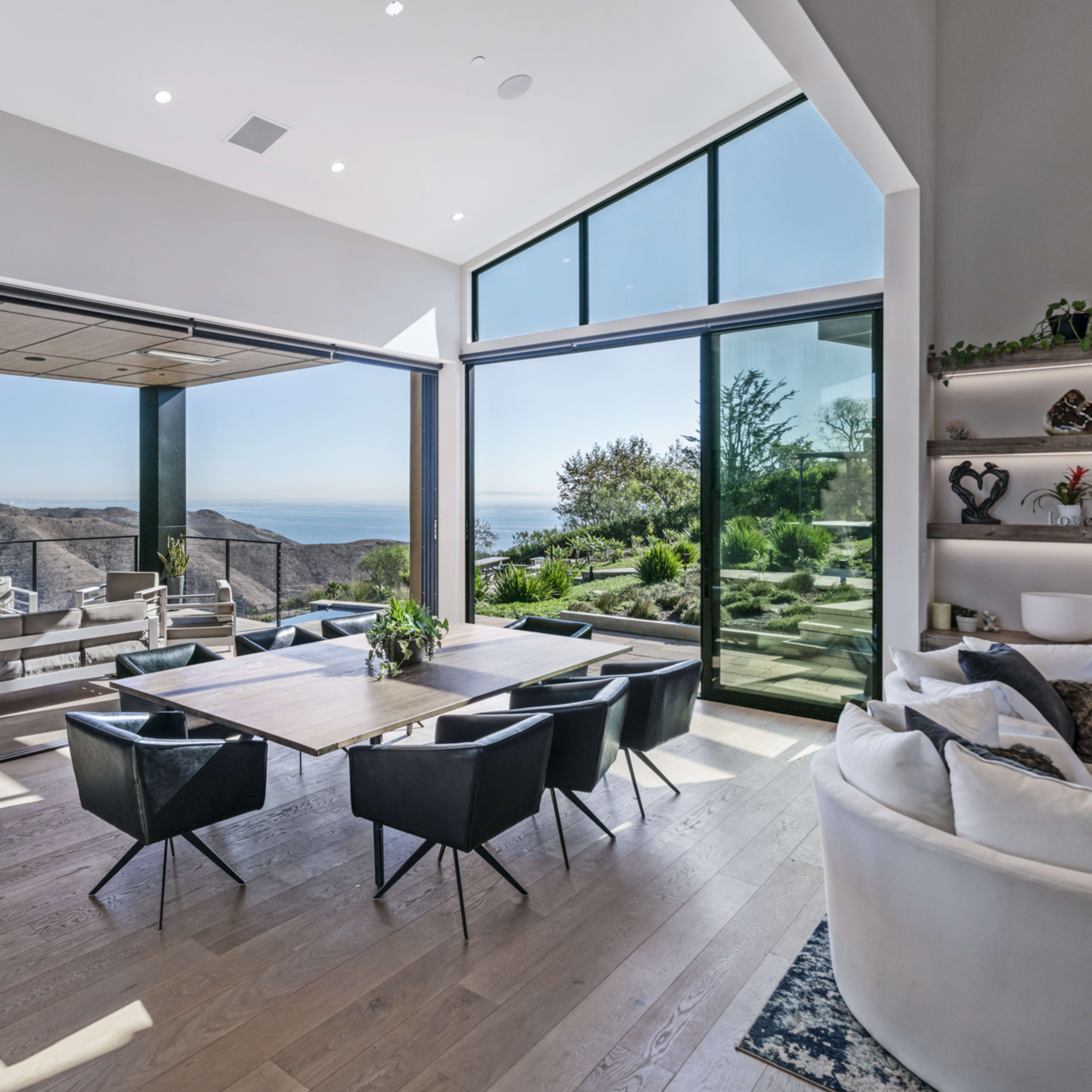 A modern dining area with large windows overlooking a scenic view of hills and a body of water.