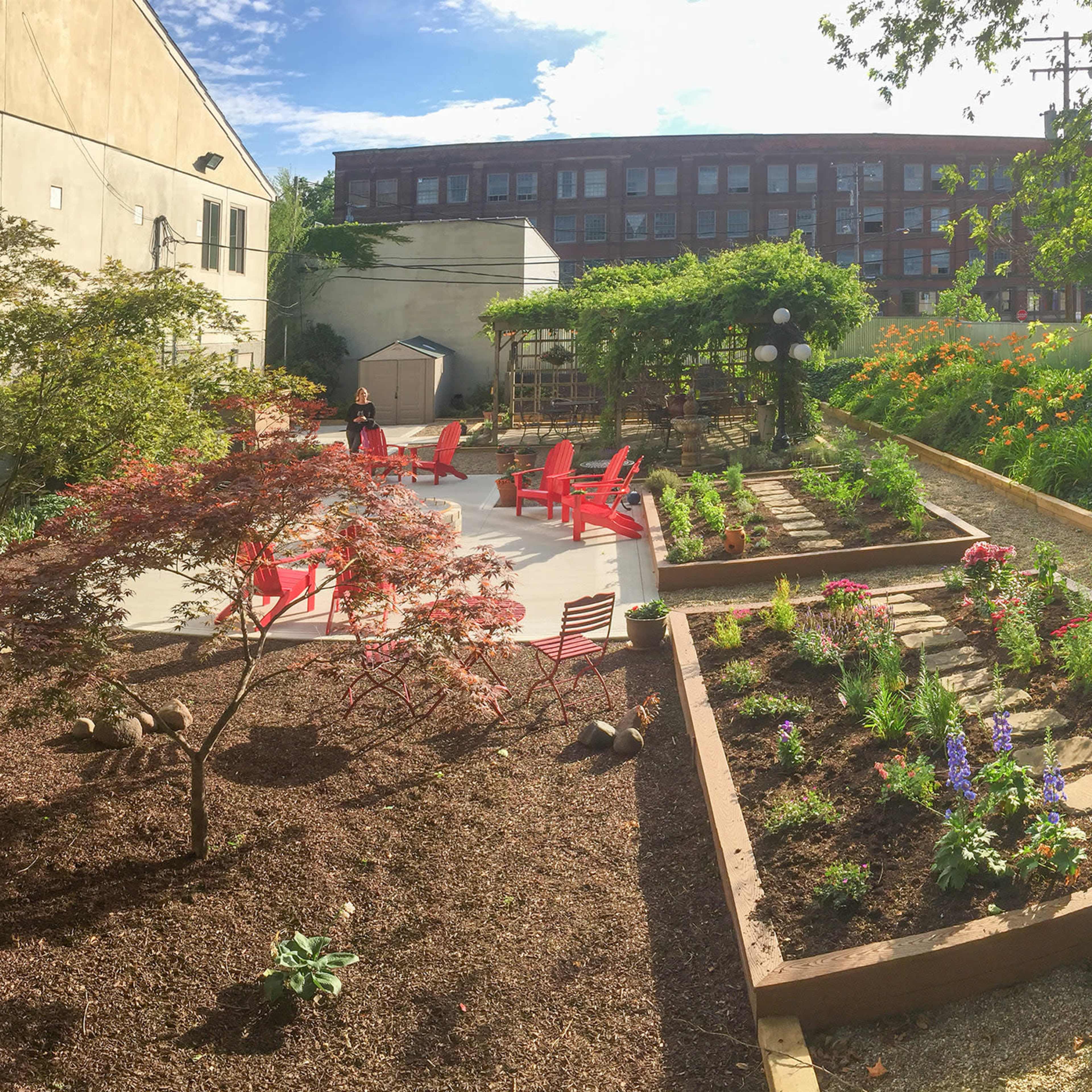 A landscaped garden featuring raised flower beds, red chairs, and a pathway bordered by greenery.