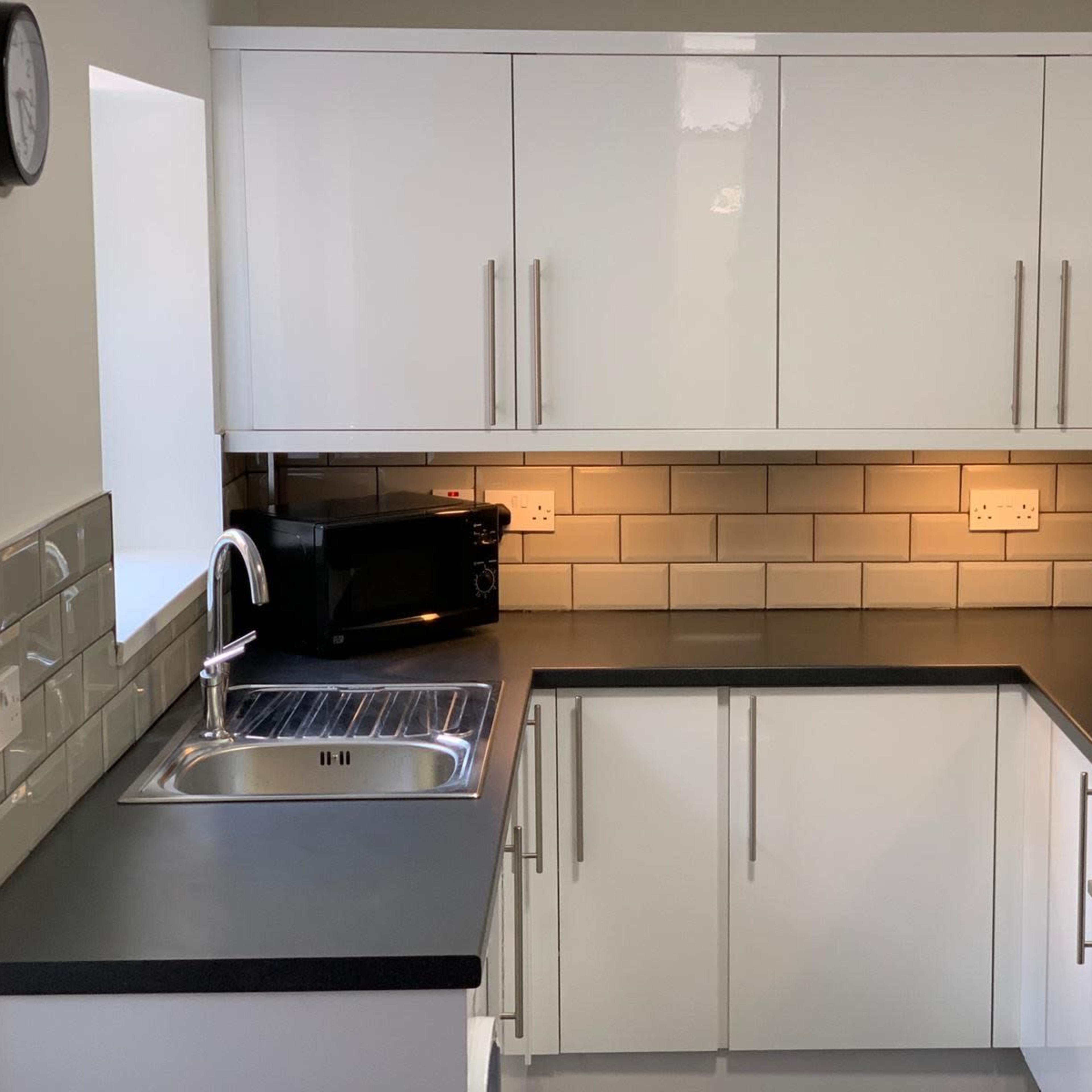 A modern kitchen features white cabinetry, a dark countertop, stainless steel appliances, and a tiled backsplash.