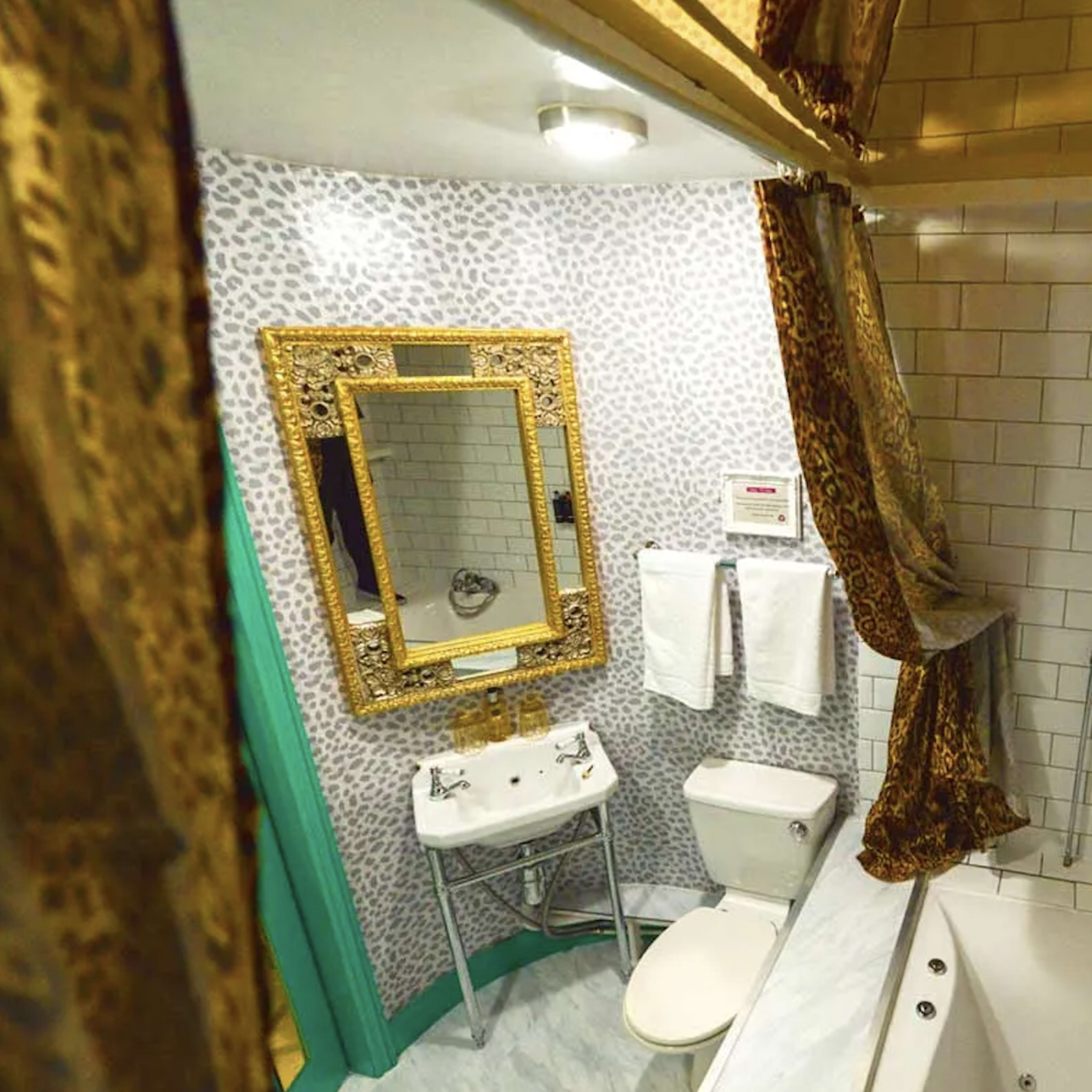 A small bathroom featuring a bathtub, a toilet, a sink with a mirror, and patterned wallpaper.