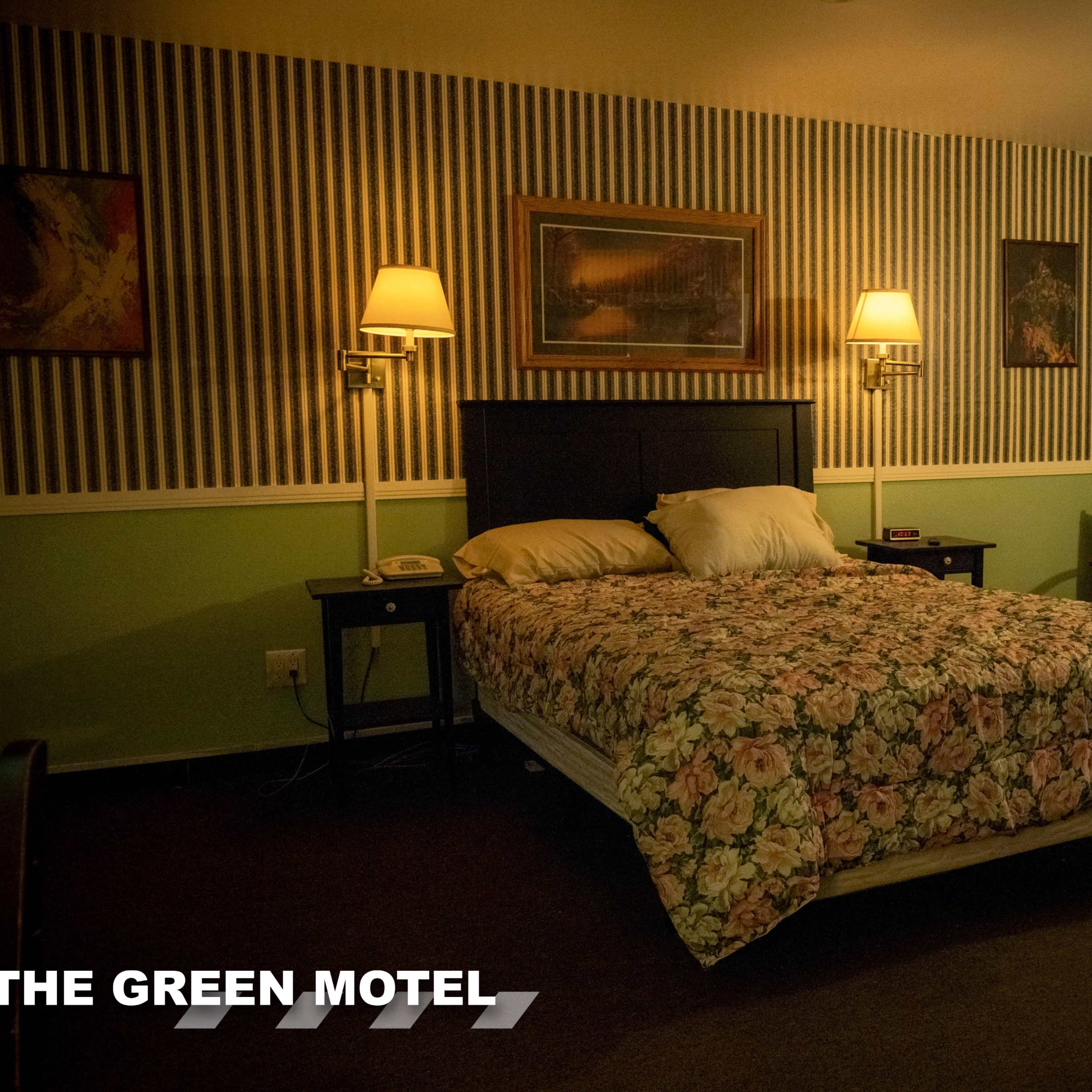 A motel room with a double bed covered in floral bedding, two wall lamps, and a chair beside a door.