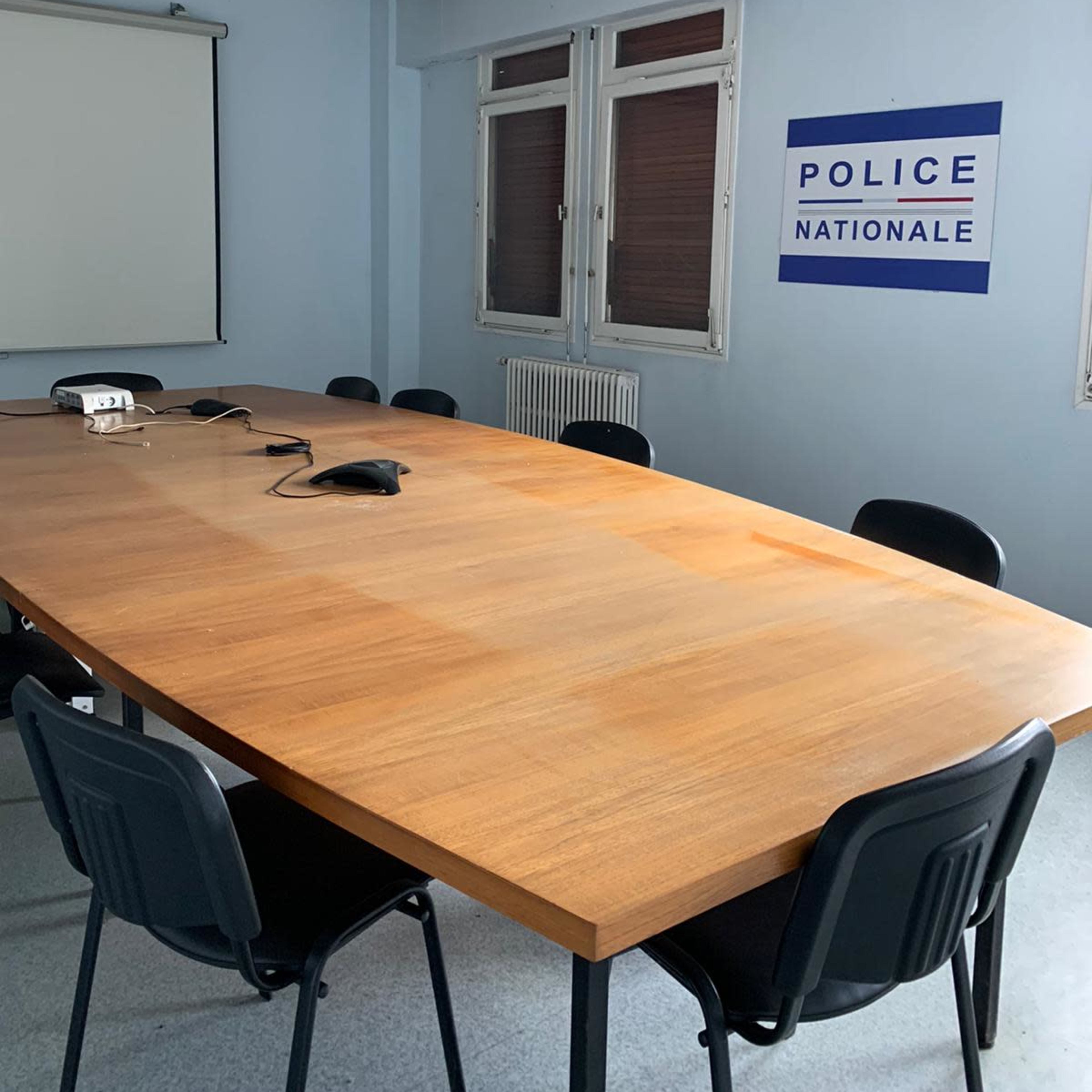 A conference room with a large wooden table surrounded by black chairs and a wall displaying a "POLICE NATIONALE" sign.