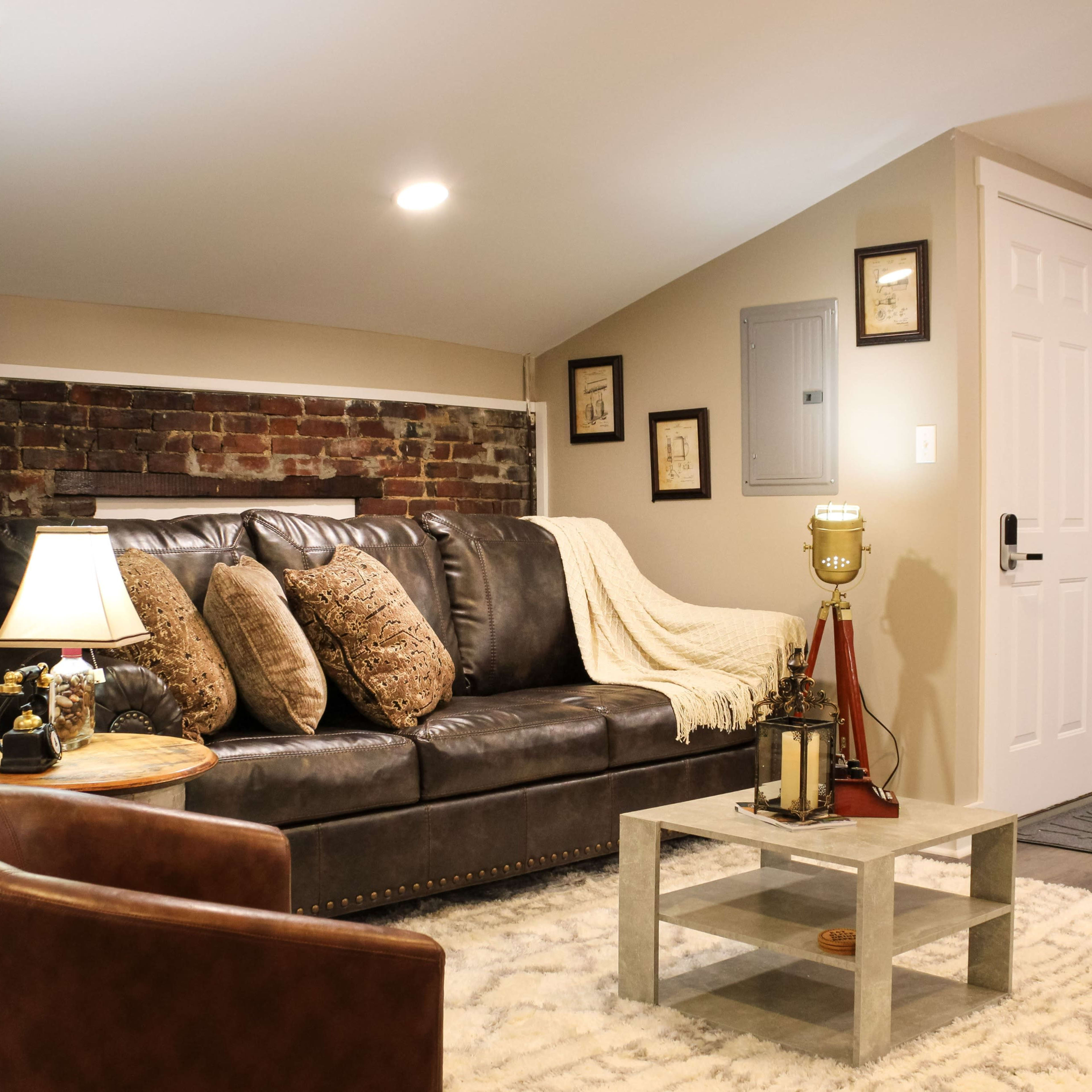 A cozy living room with a brown leather sofa, a small coffee table, a lamp, and exposed brick walls.