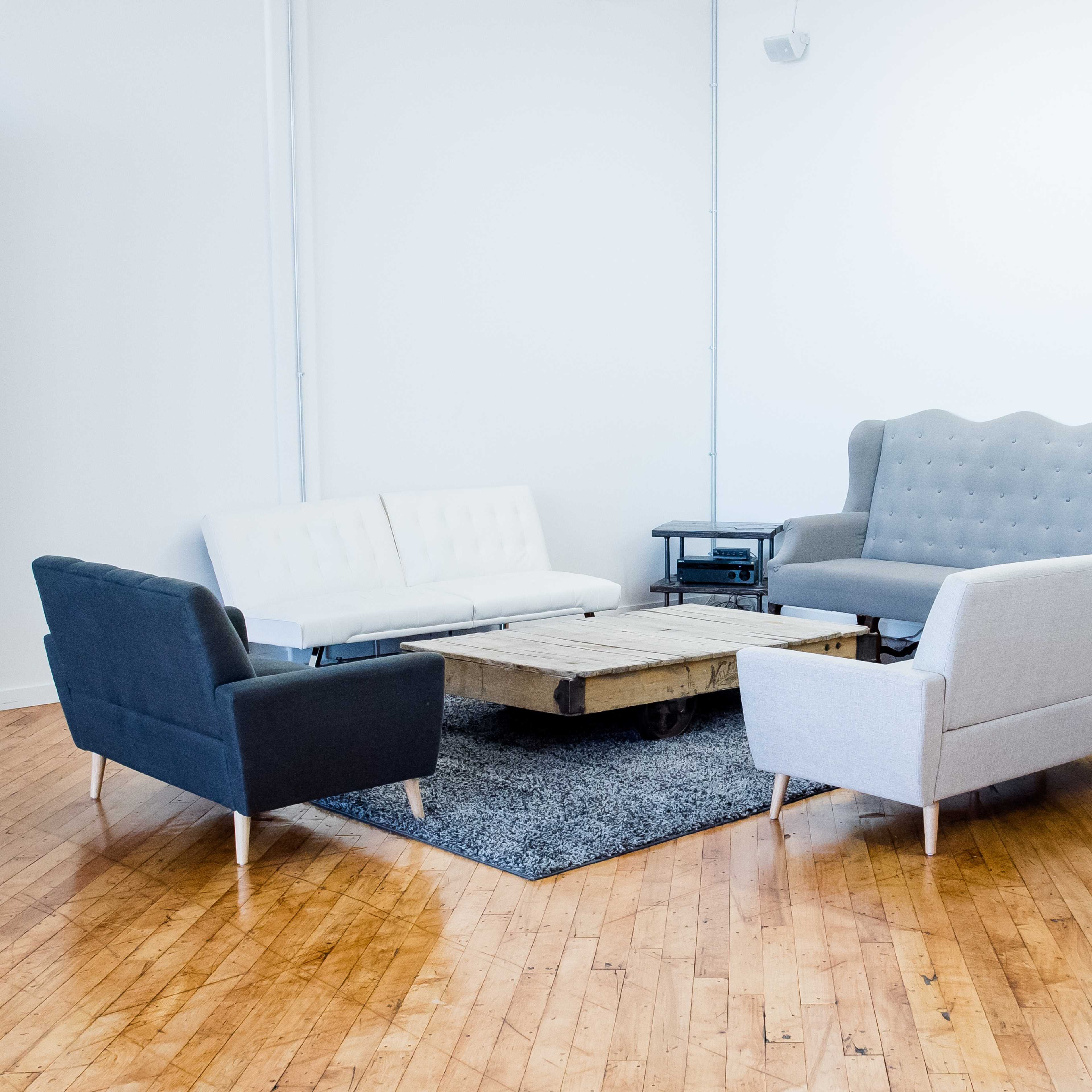 A seating arrangement with four sofas and a wooden coffee table on a dark rug in a room with light-colored walls and hardwood floors.
