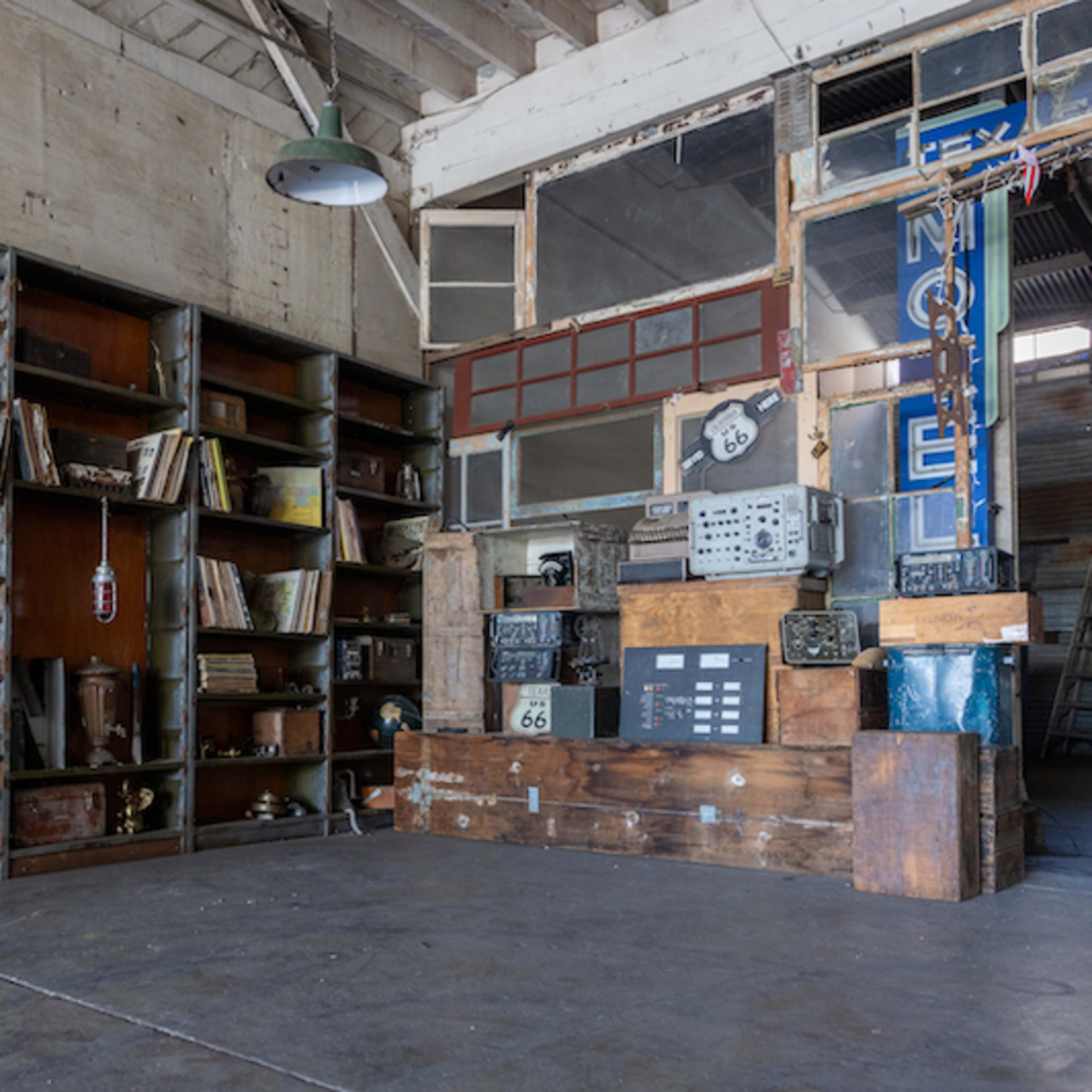 A spacious room featuring wooden shelves filled with books and various items, alongside a large wooden display structure against an industrial backdrop.
