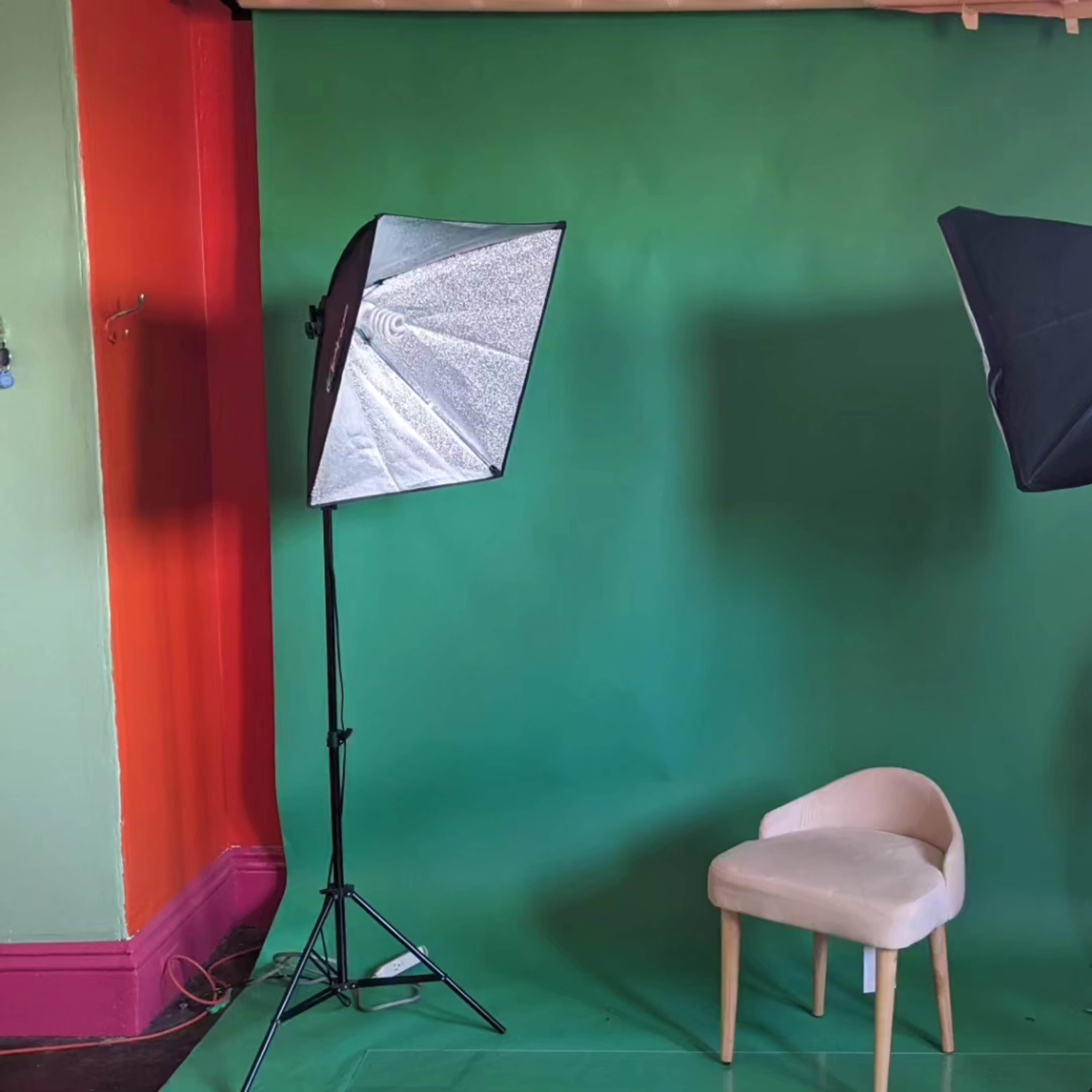 A green backdrop with two softbox lights and a single light-colored chair positioned in front.