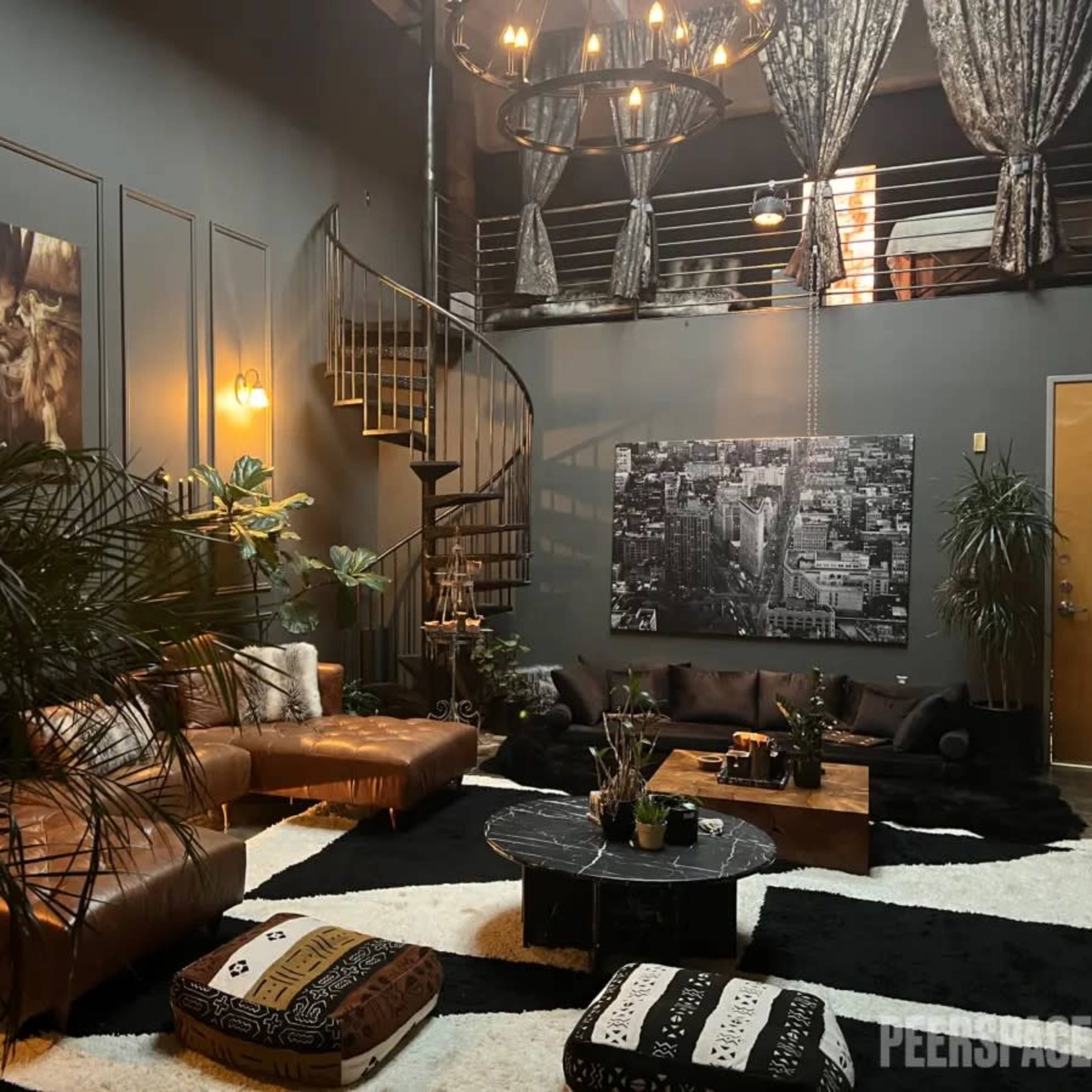 A modern living room with a spiral staircase, dark walls, leather seating, and a large black and white photograph on the wall.