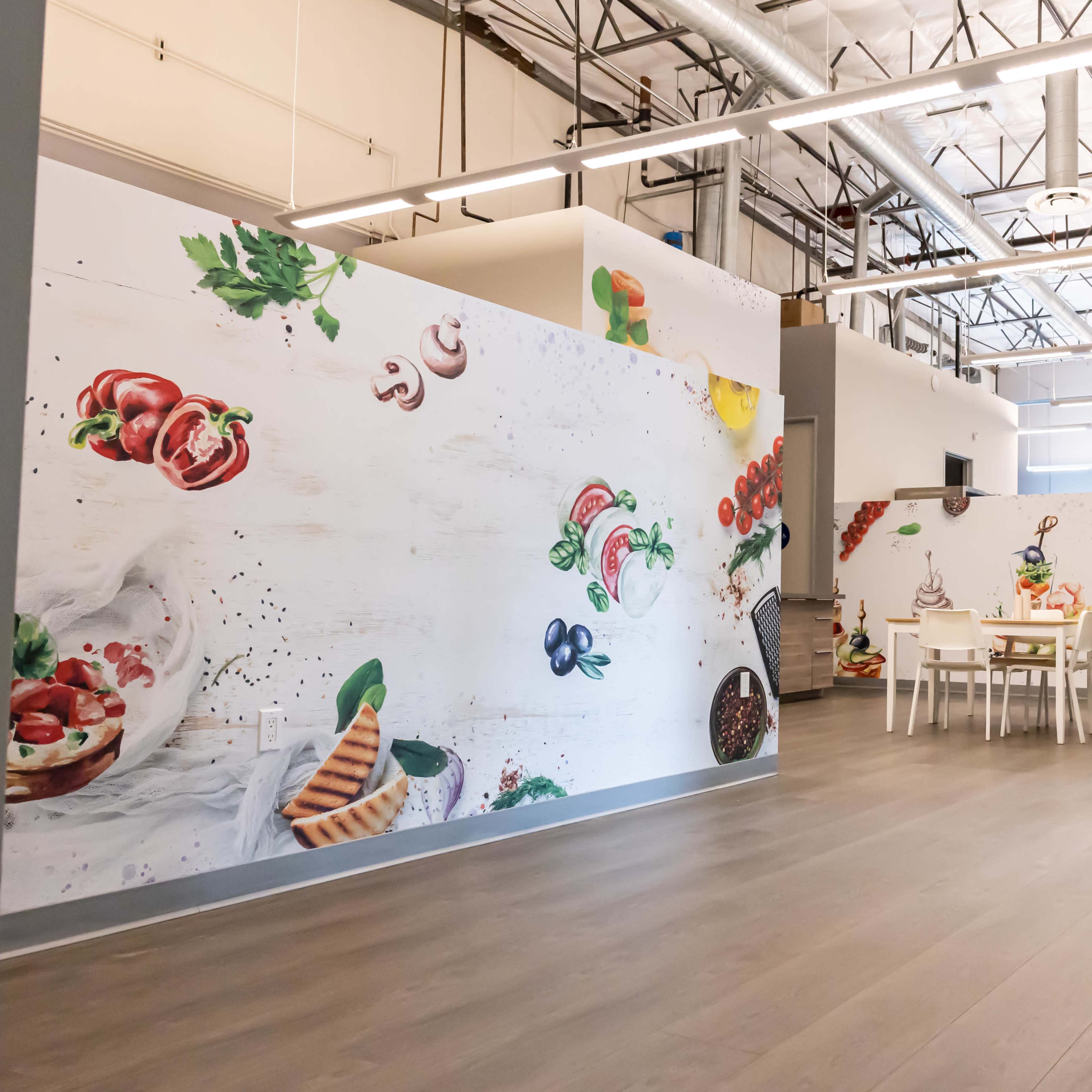 A spacious room with large murals of food items on the walls and a dining area featuring a white table and chairs.